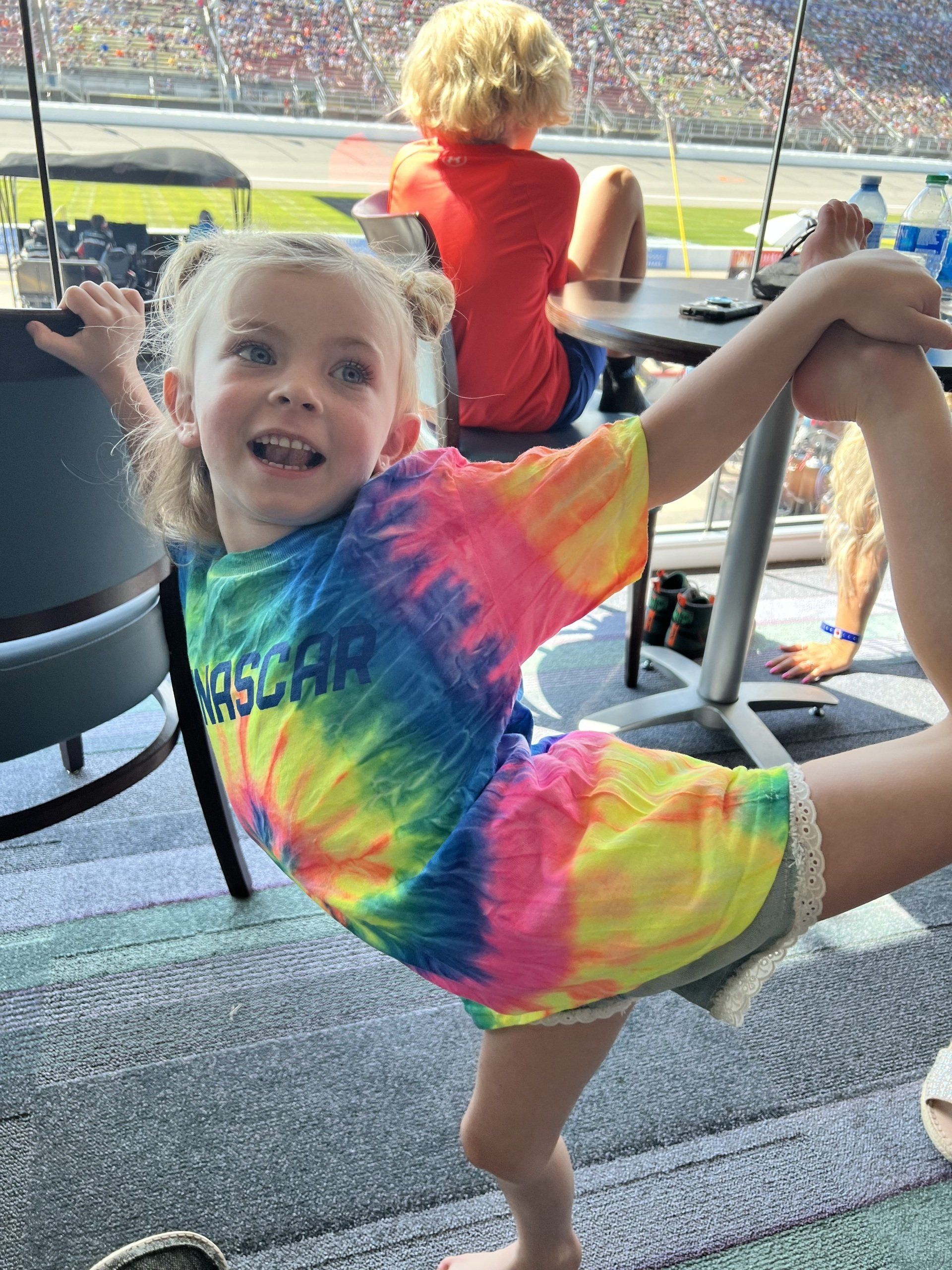 A little girl in a tie dye shirt is doing a split