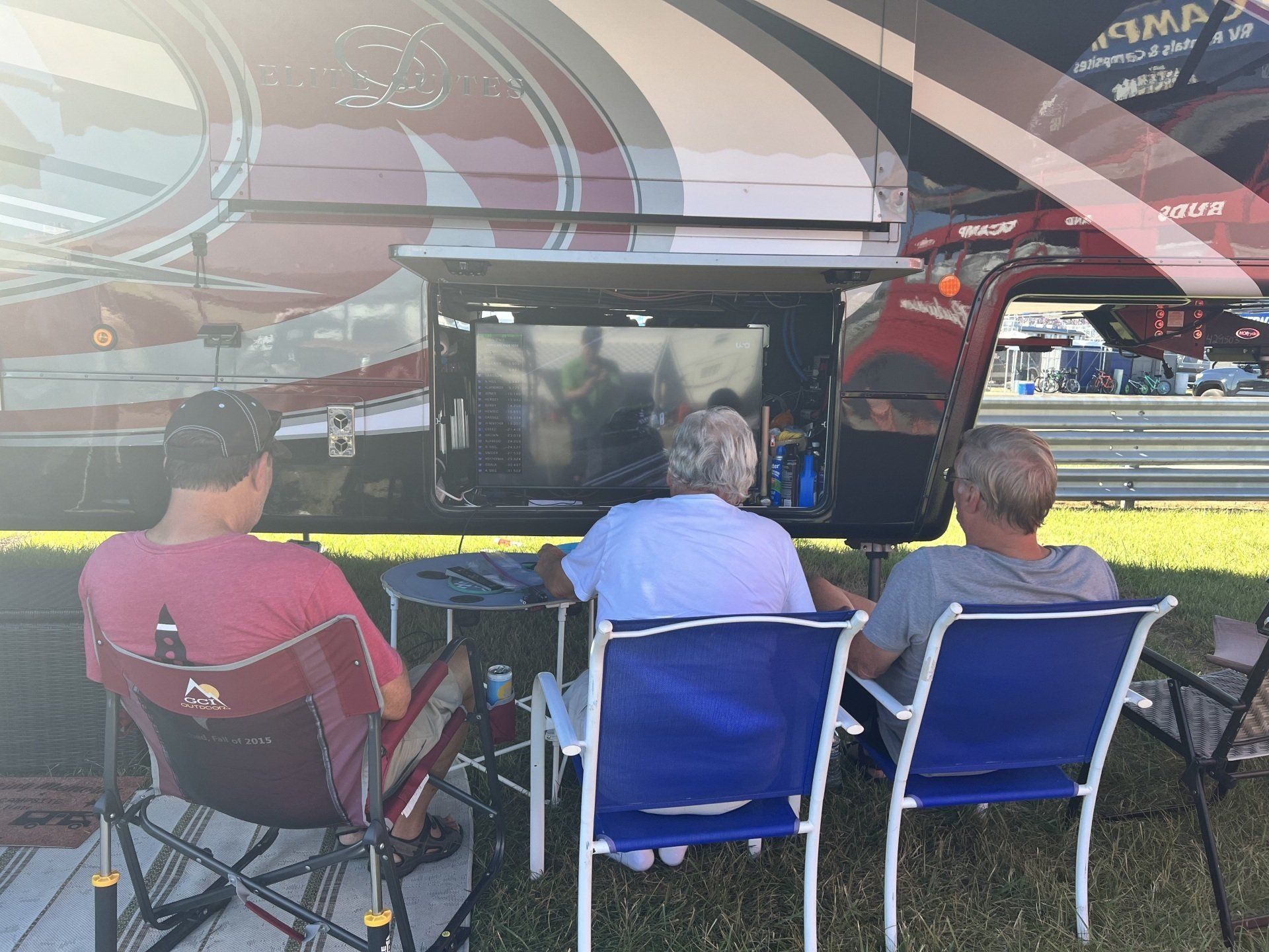 Three people are sitting in chairs in front of a rv