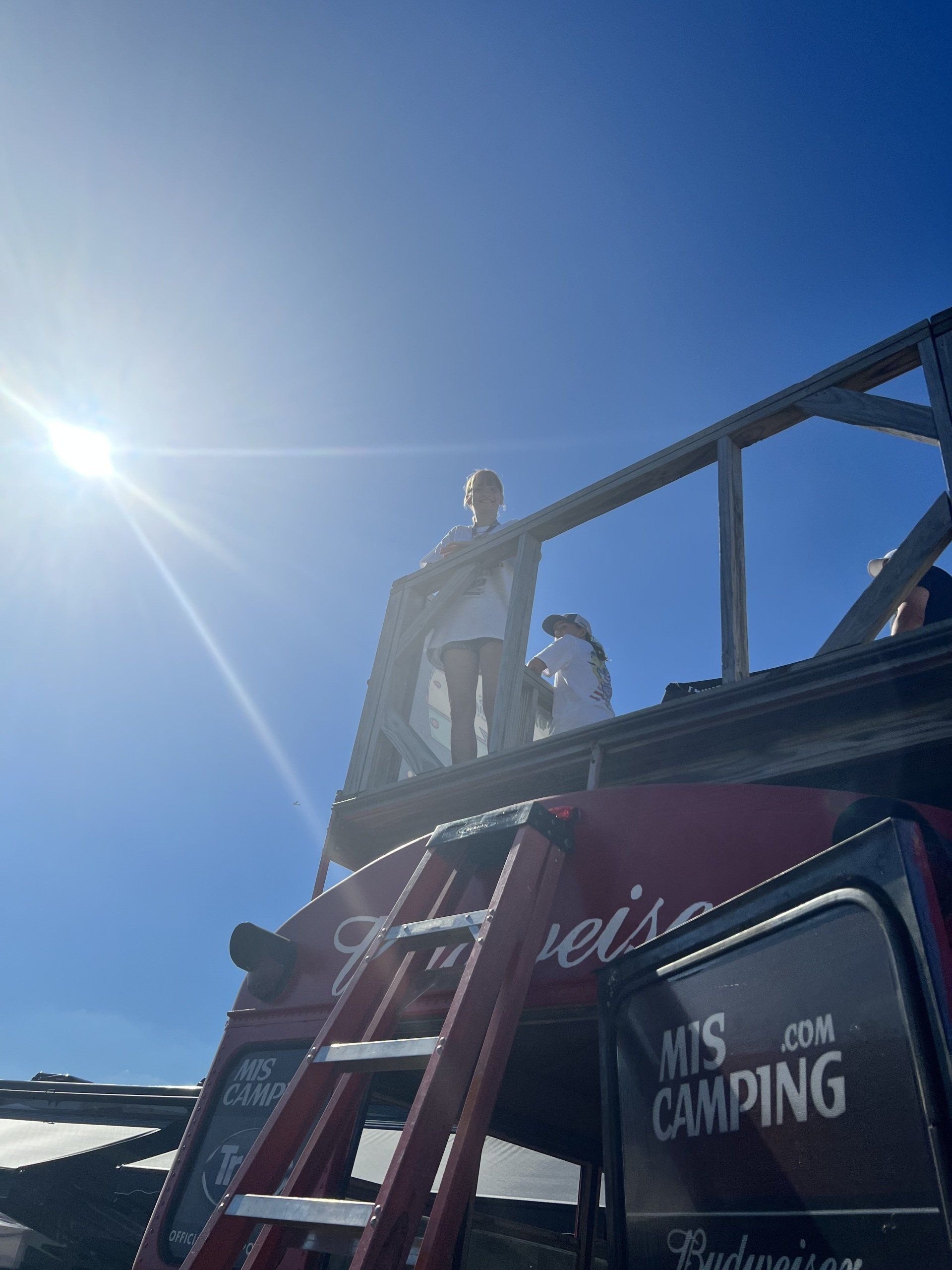 A man standing on top of a red truck that says mis camping on the side