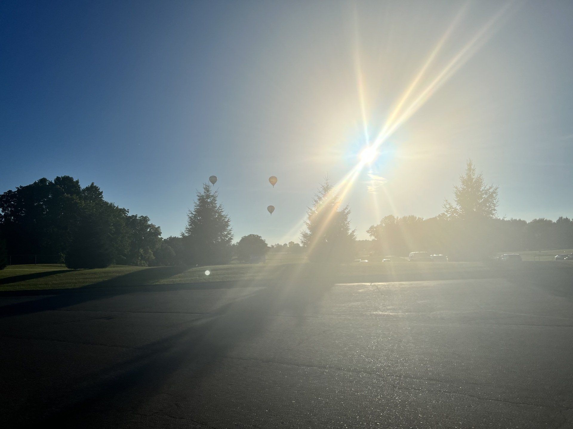The sun is shining brightly over a parking lot with trees in the background.