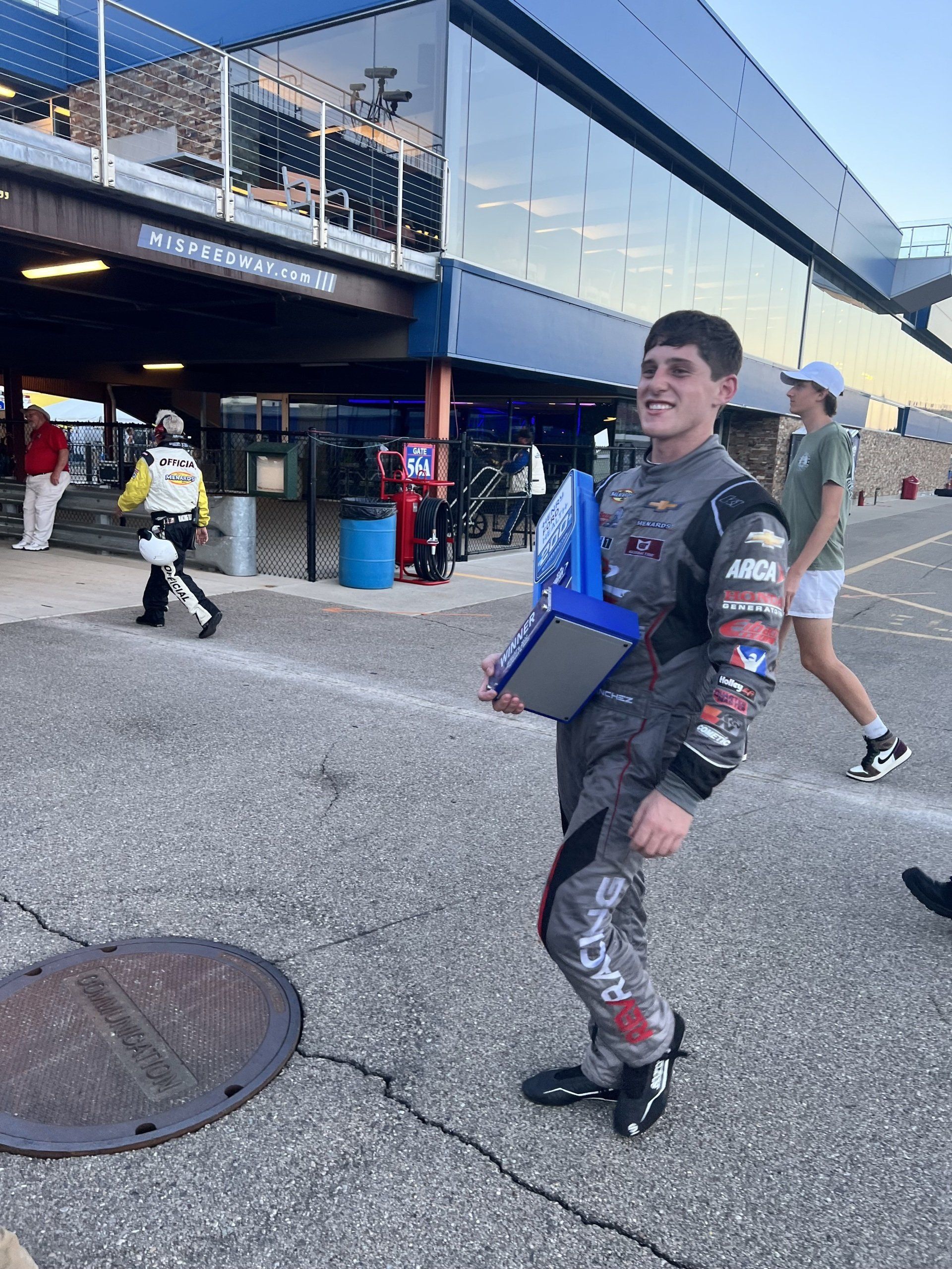 A man in a race suit is standing in front of a building
