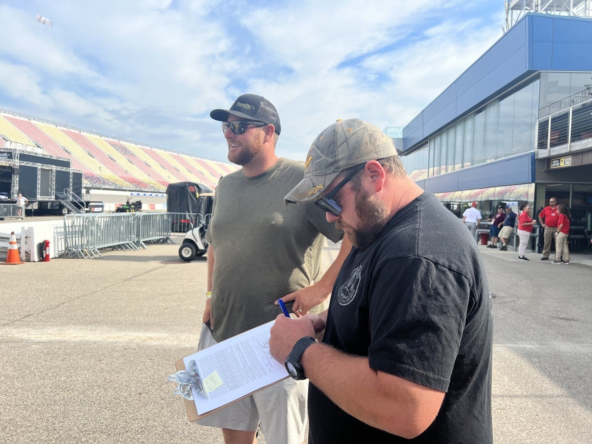 Two men are standing next to each other and one is writing on a clipboard.