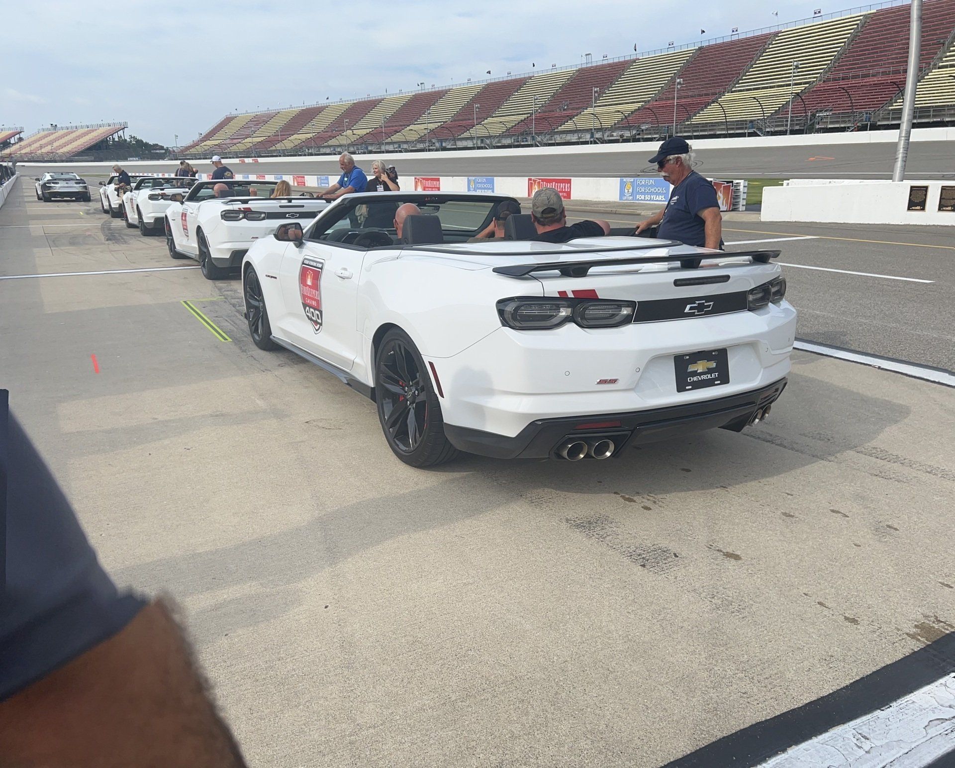 A row of white cars are parked on a race track