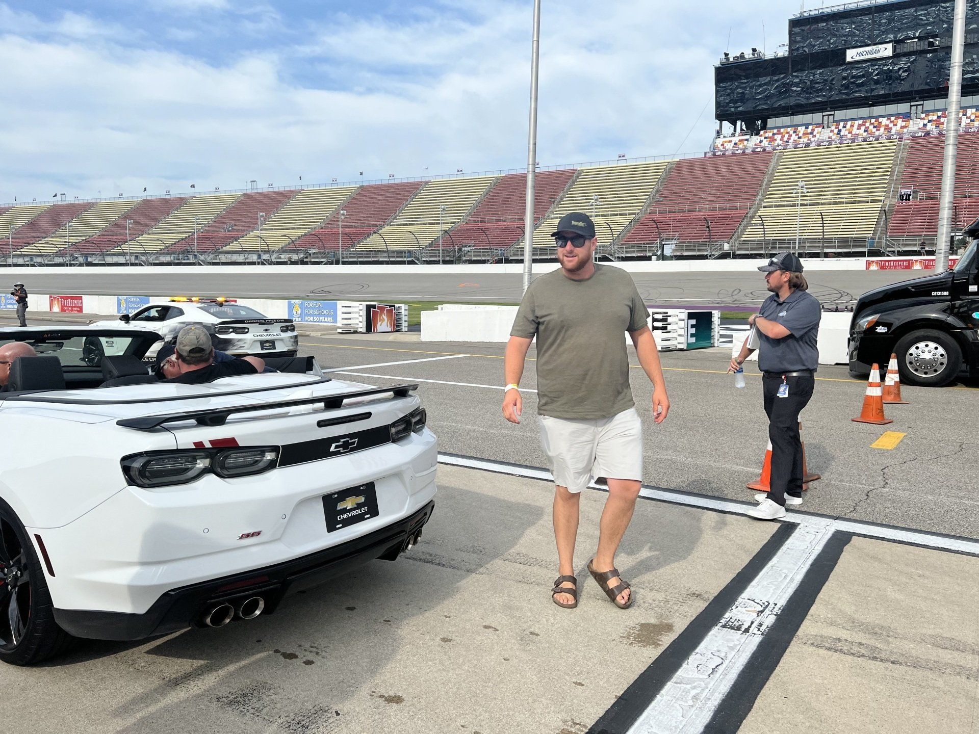 A man is standing next to a white convertible on a race track.