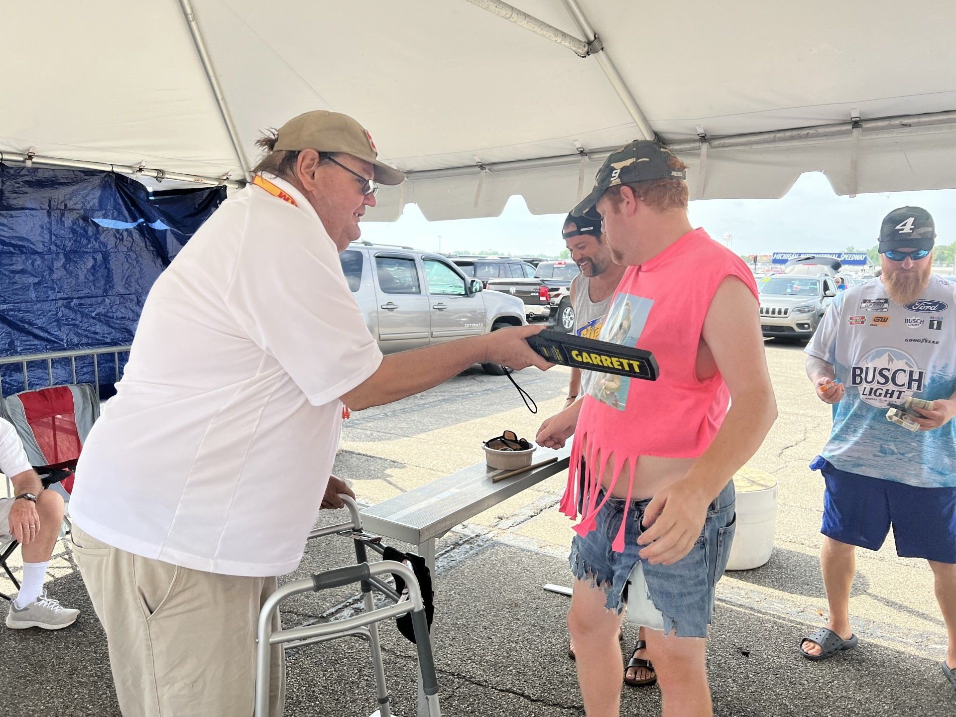A man in a pink shirt is talking to another man under a tent