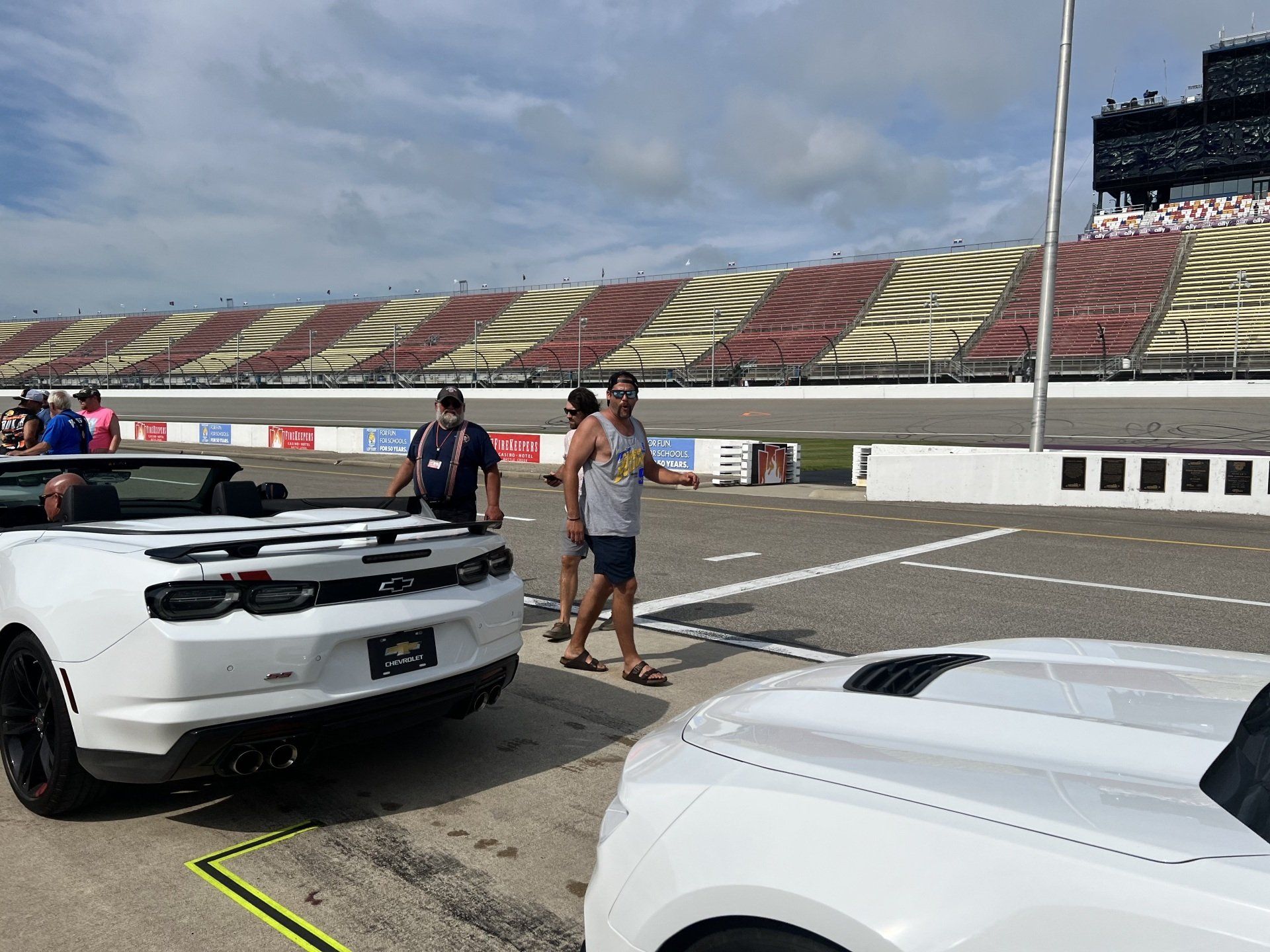 A group of people are standing next to two white cars on a race track.