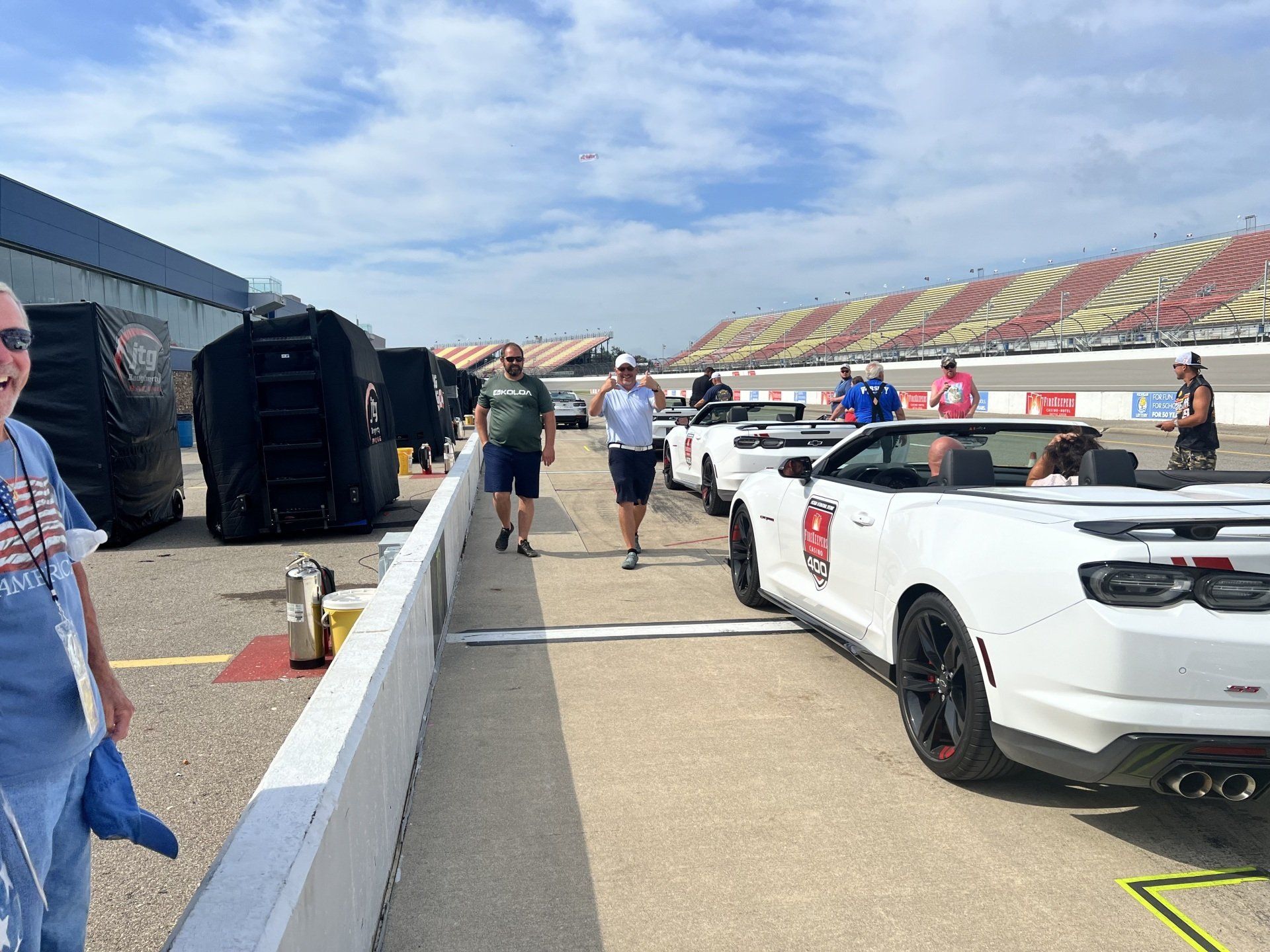 A man is standing next to a white convertible car on a race track.