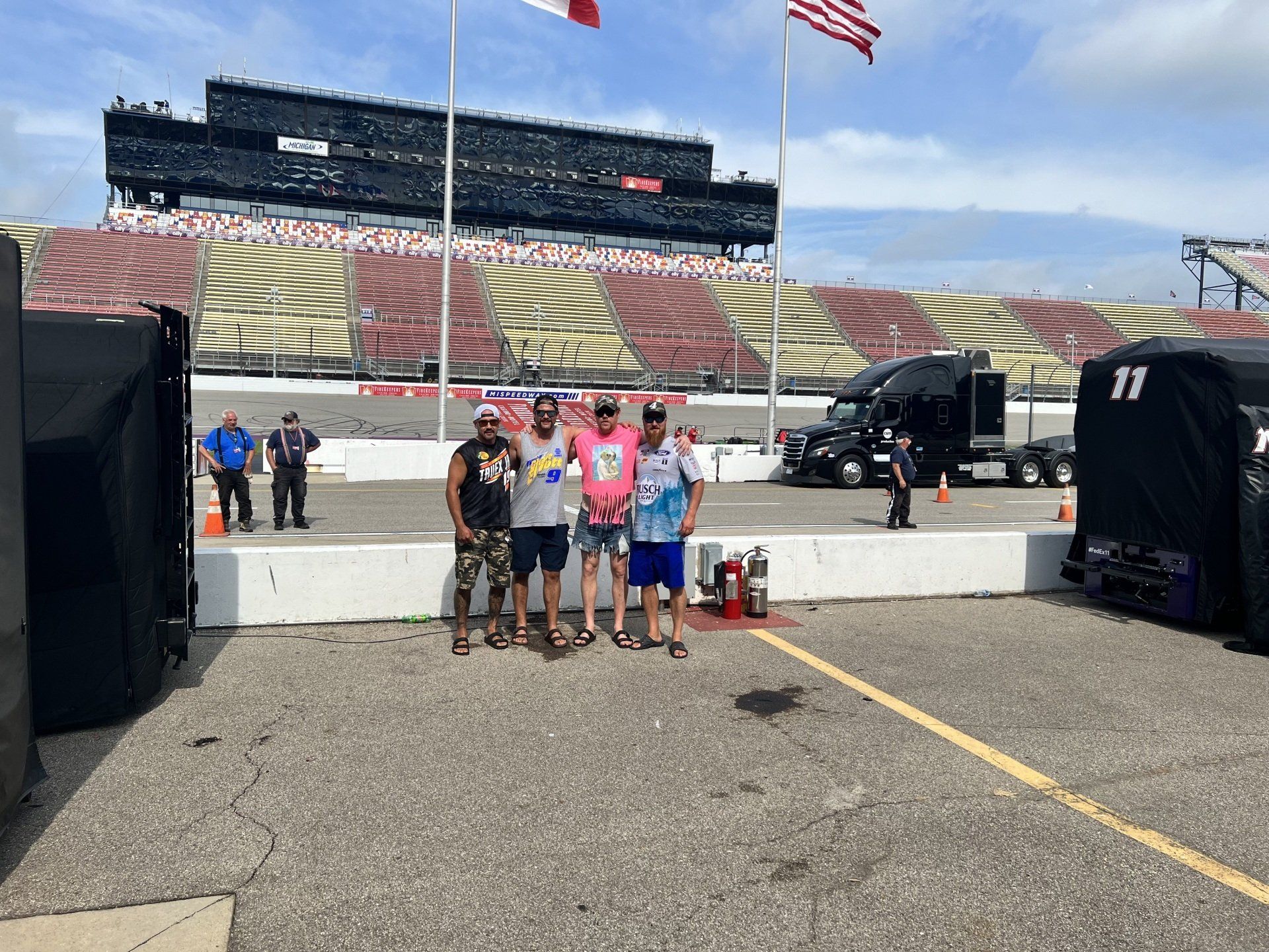 A group of men are standing in a parking lot at a race track.
