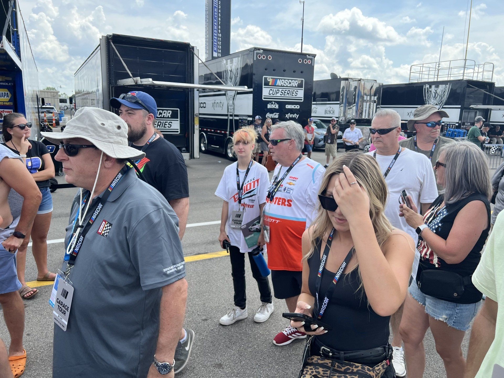 A group of people are standing in a parking lot looking at their phones.