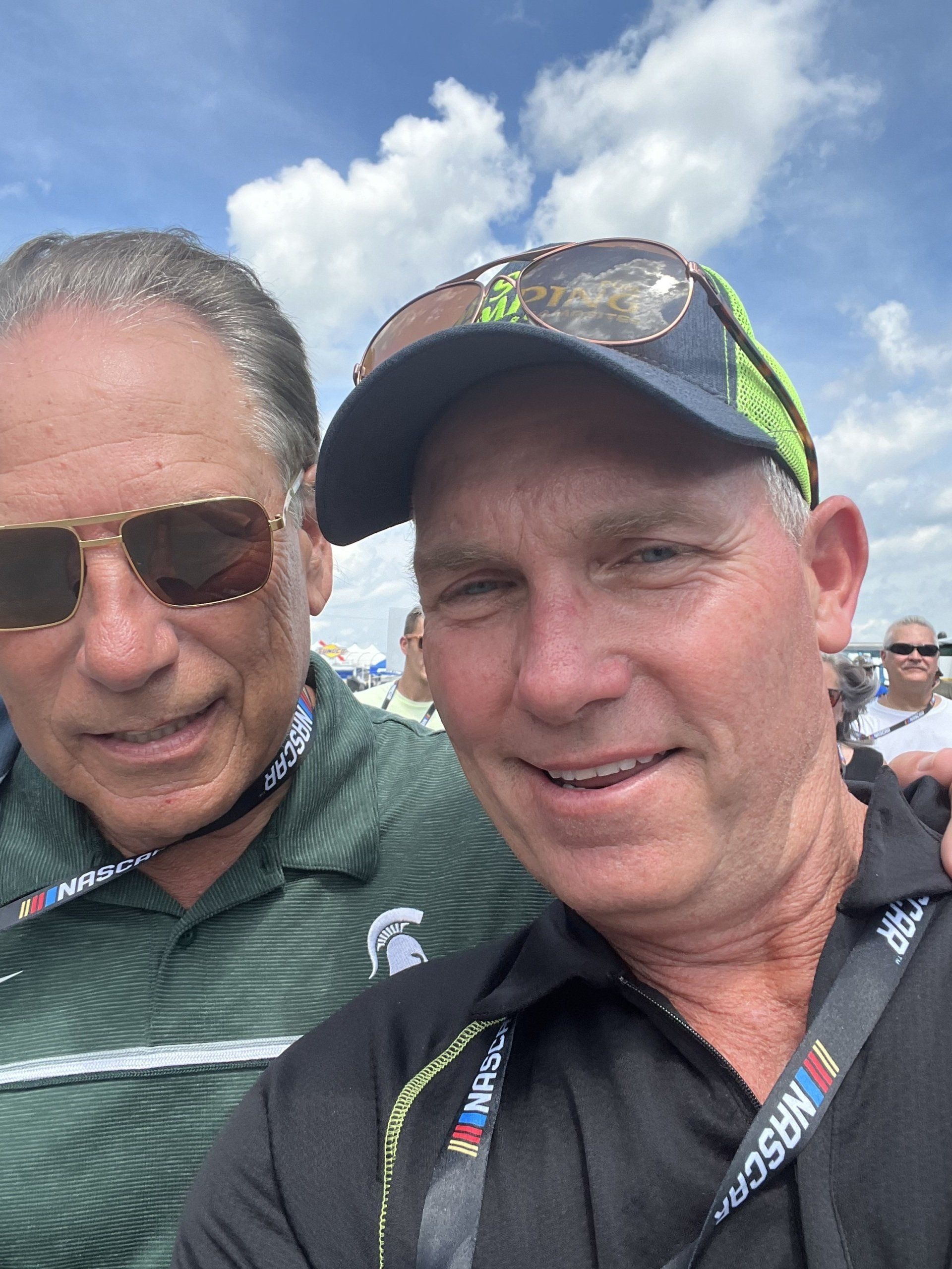 Two men are posing for a picture and one has a nascar lanyard around his neck