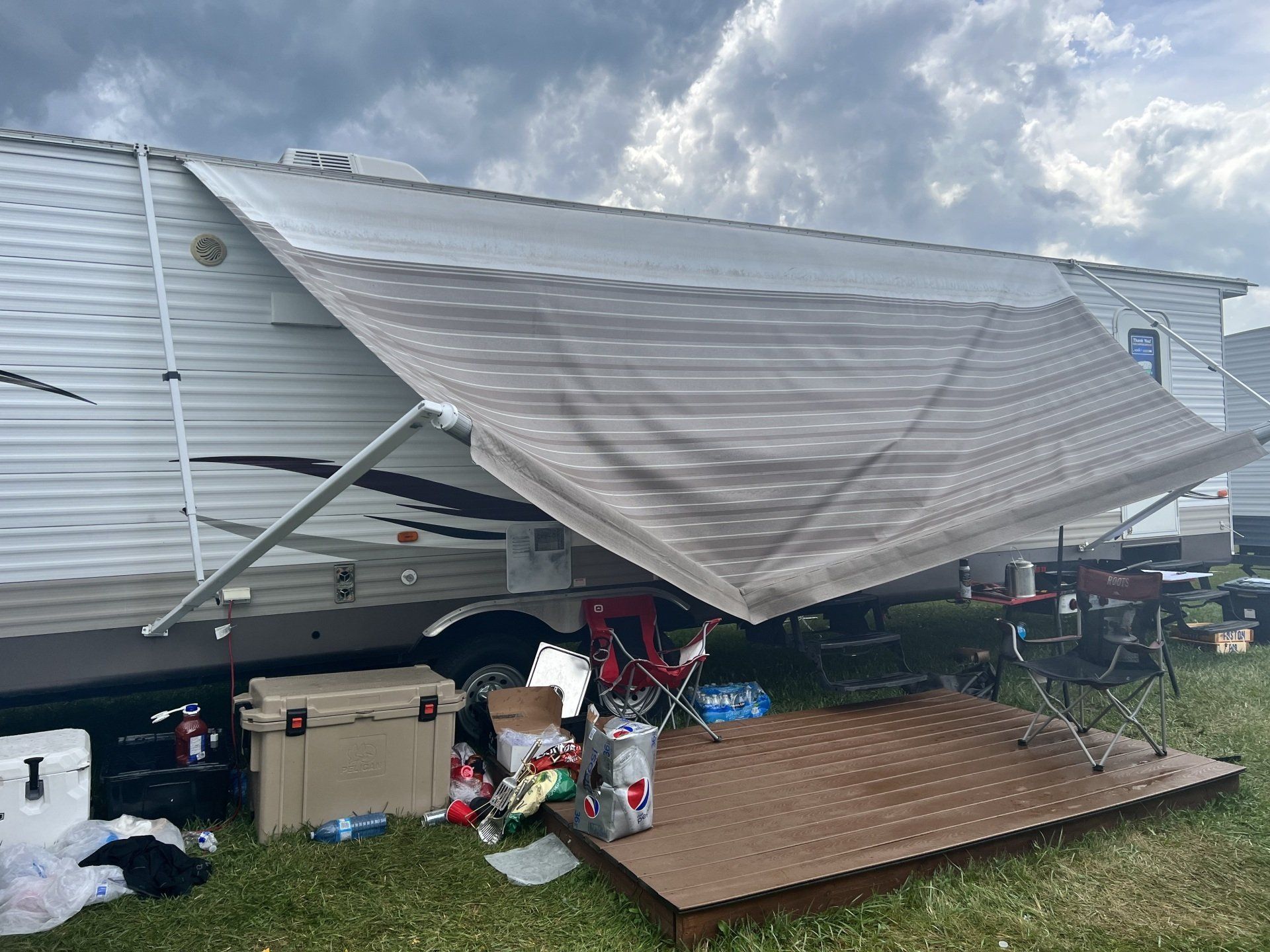 A rv with a broken awning is parked in a field.