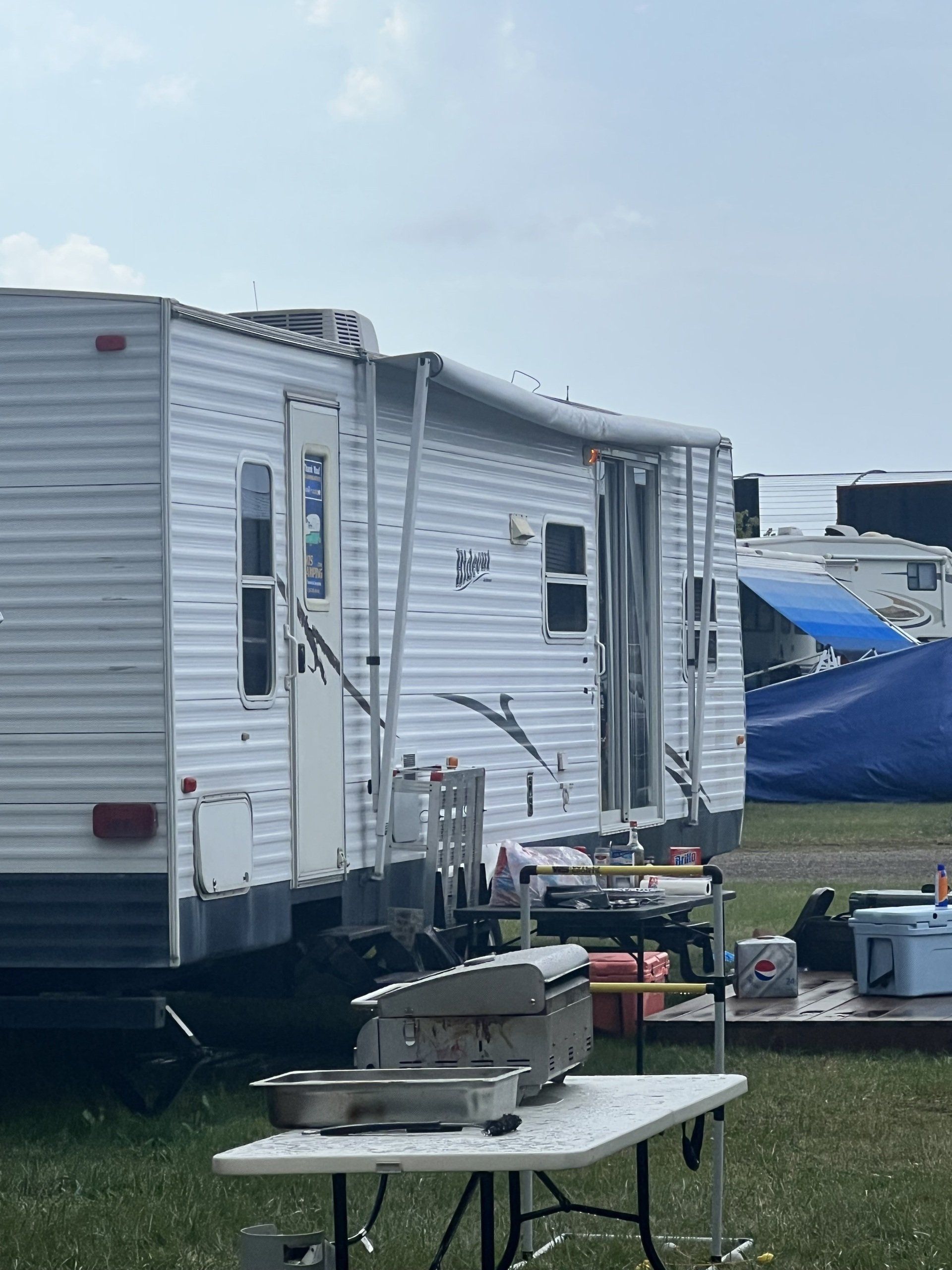 A white trailer is parked next to a table with a grill on it.