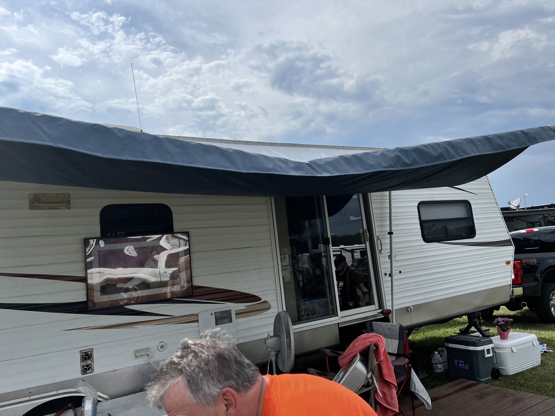 A man in an orange shirt is standing in front of a trailer.
