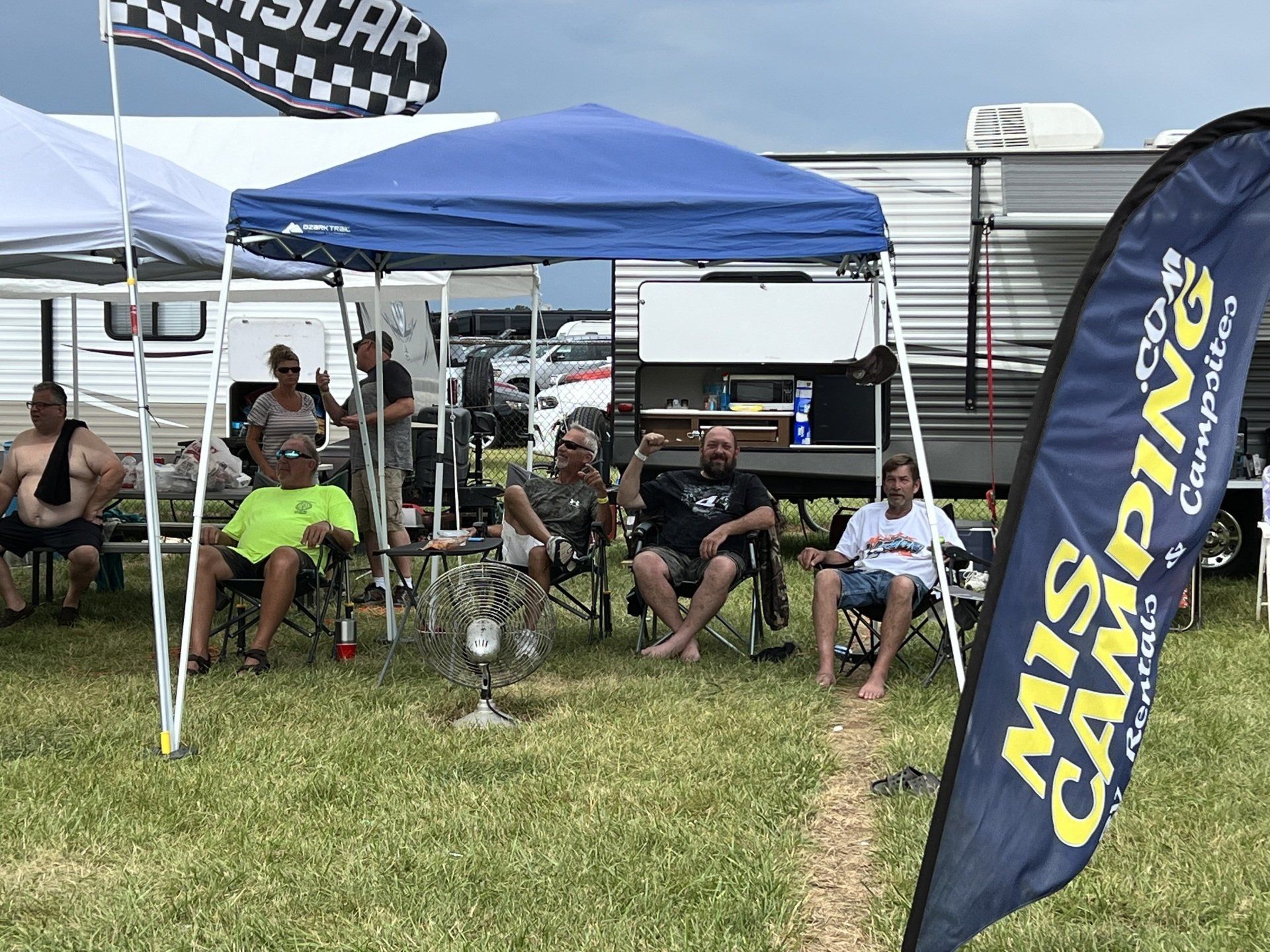A group of people are sitting under tents in a field.