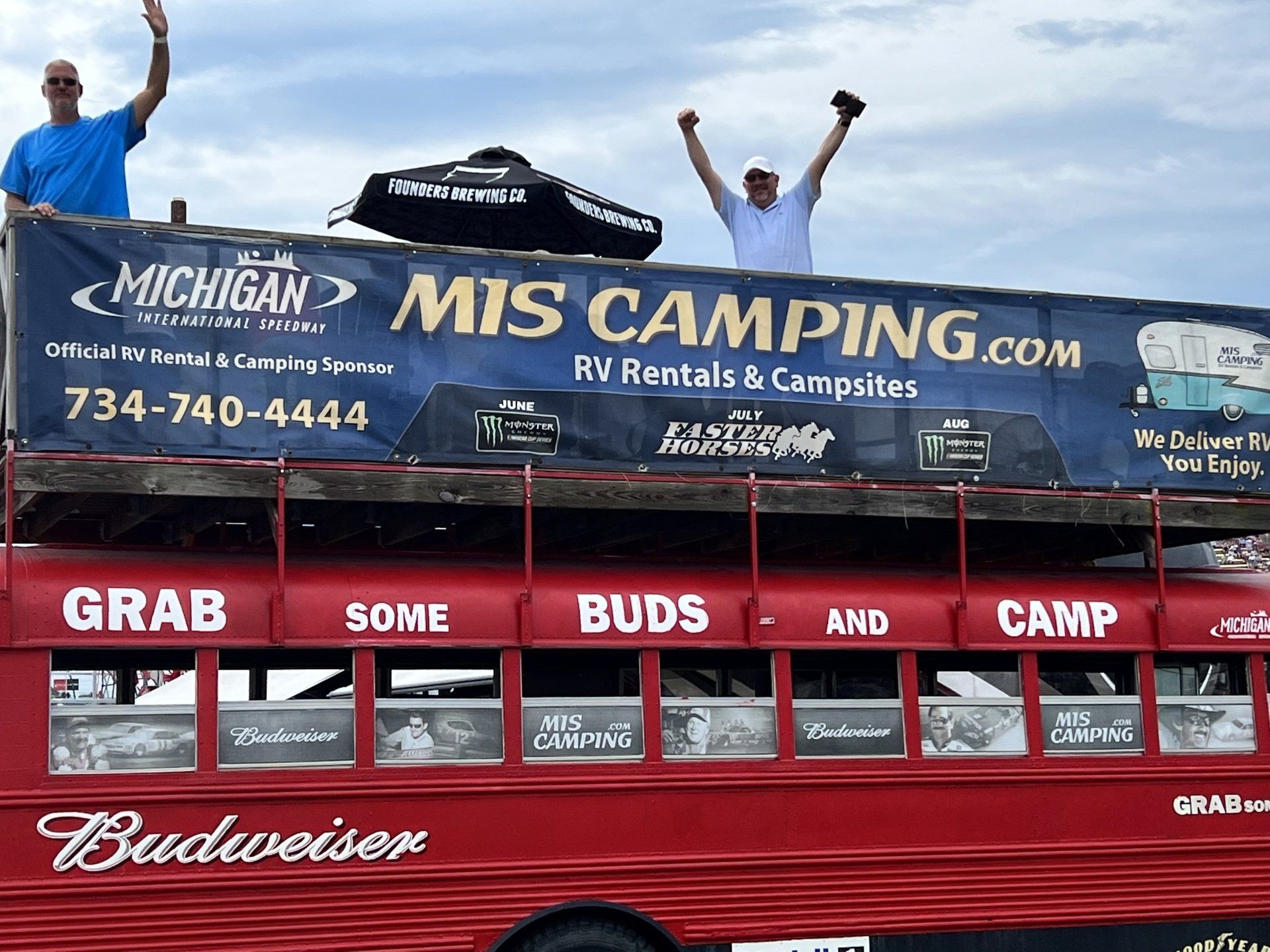 Two men standing on top of a red bus that says mis camping.com