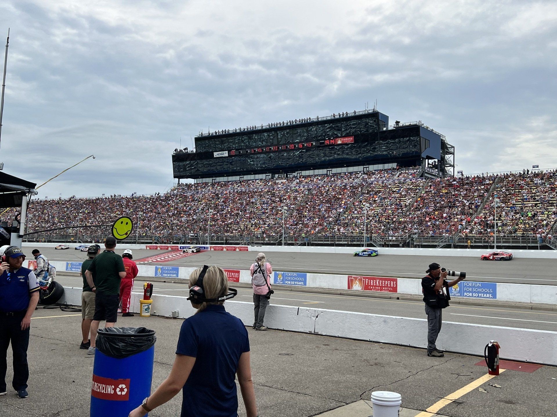 A race track with a large crowd watching and a blue barrel that says racing on it