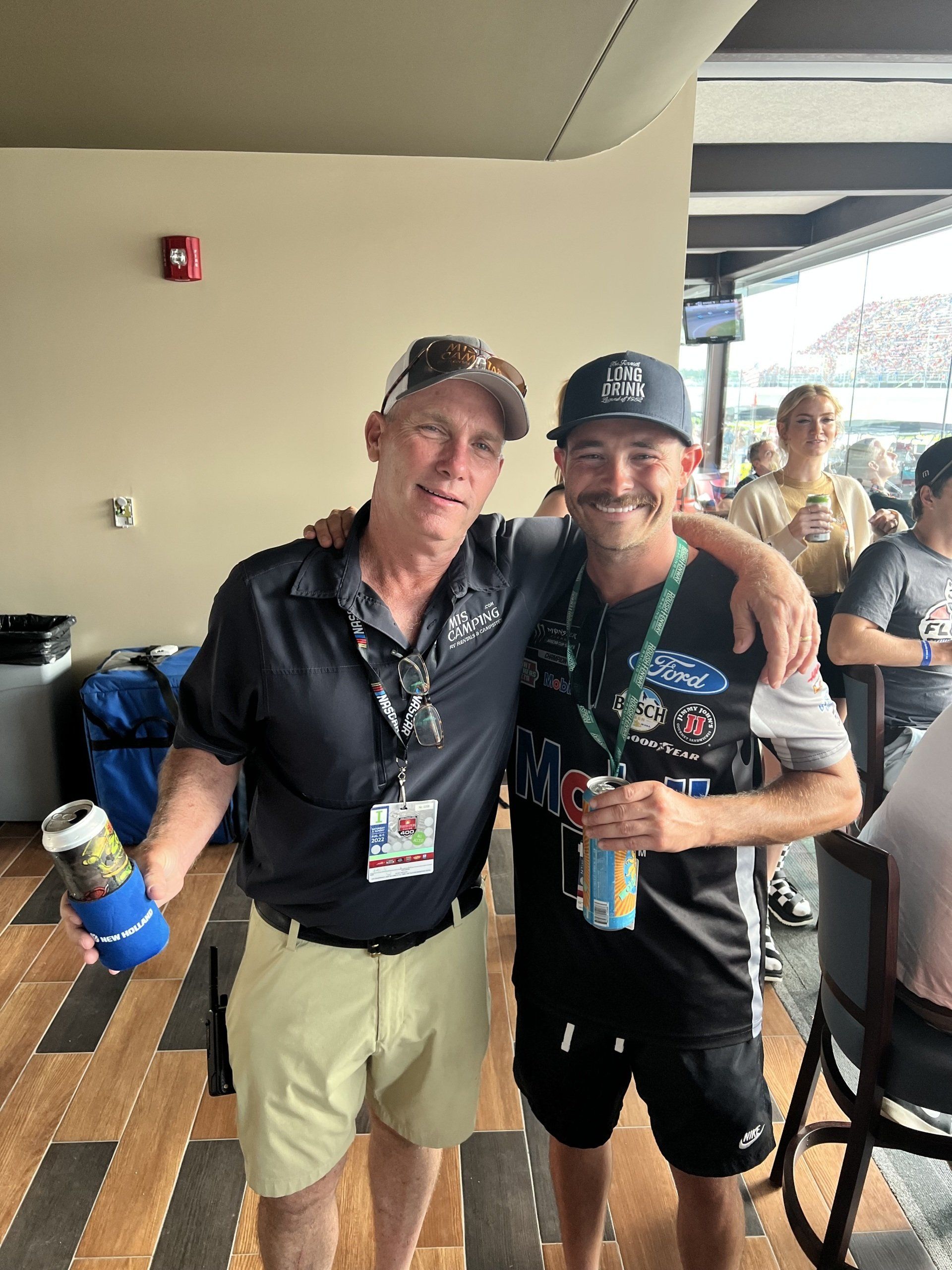 Two men are posing for a picture in a room . one of the men is wearing a ford shirt.