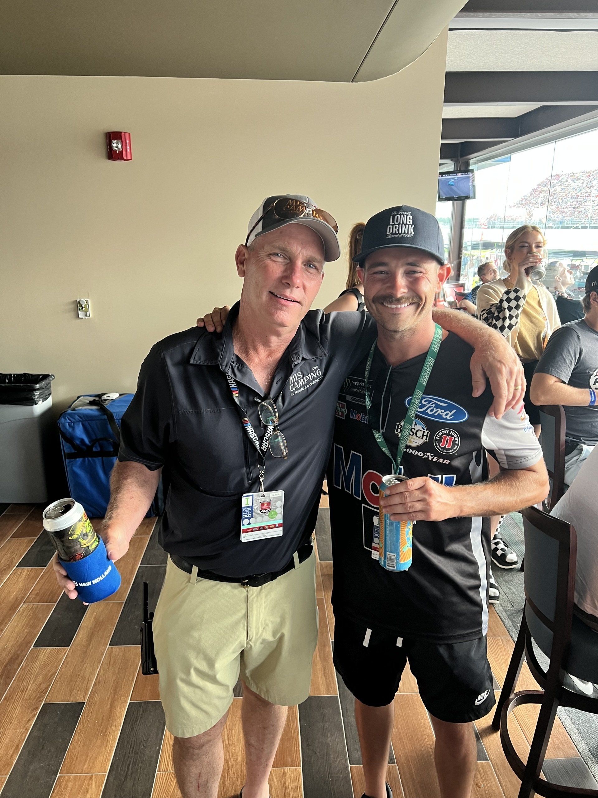 Two men are posing for a picture and one of them is holding a can of beer.