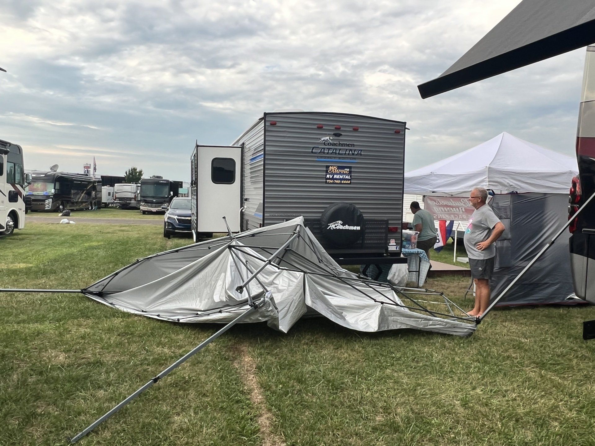 A man is standing next to a tent that has fallen in a field.