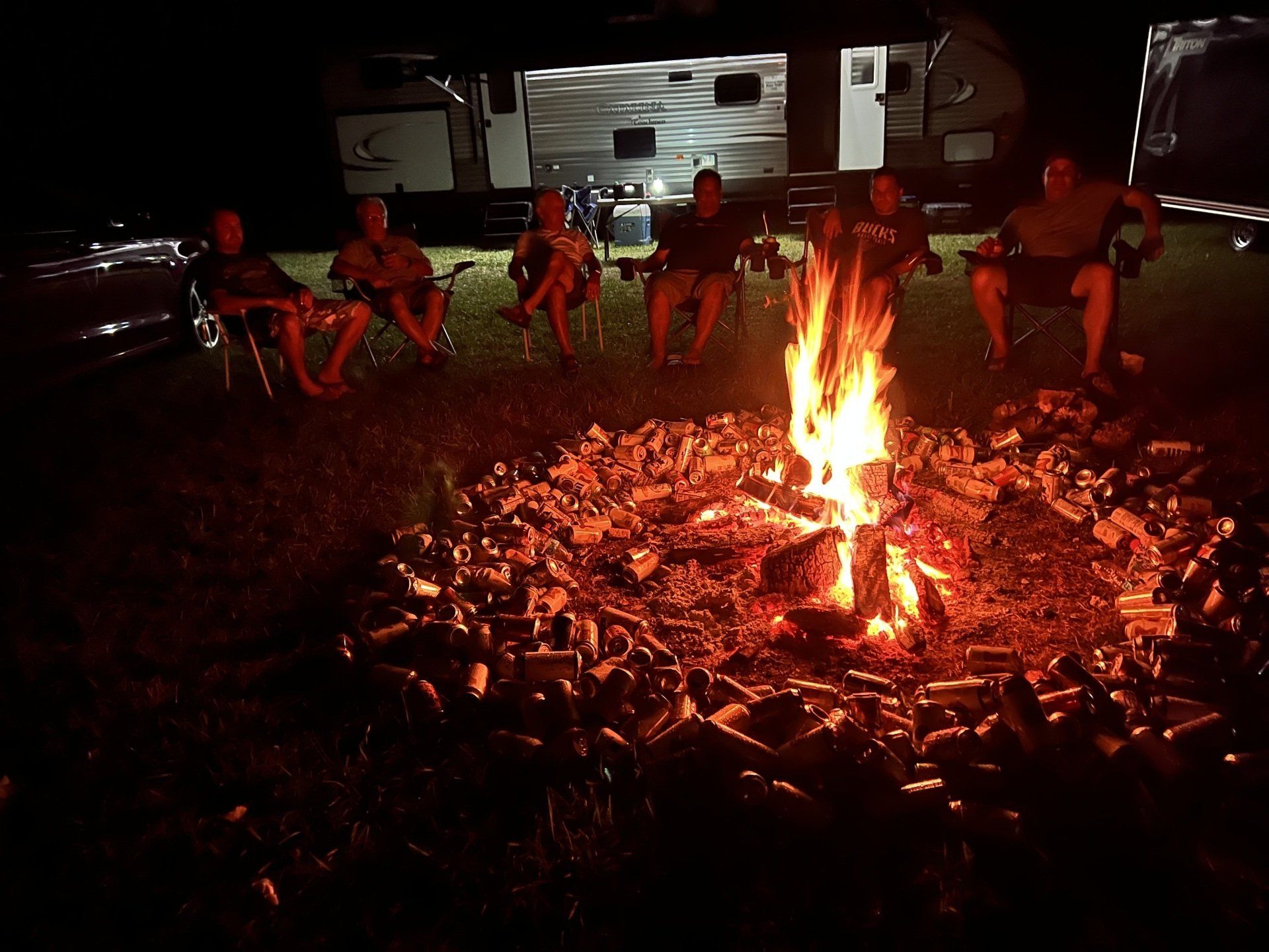 A group of people are sitting around a campfire at night.