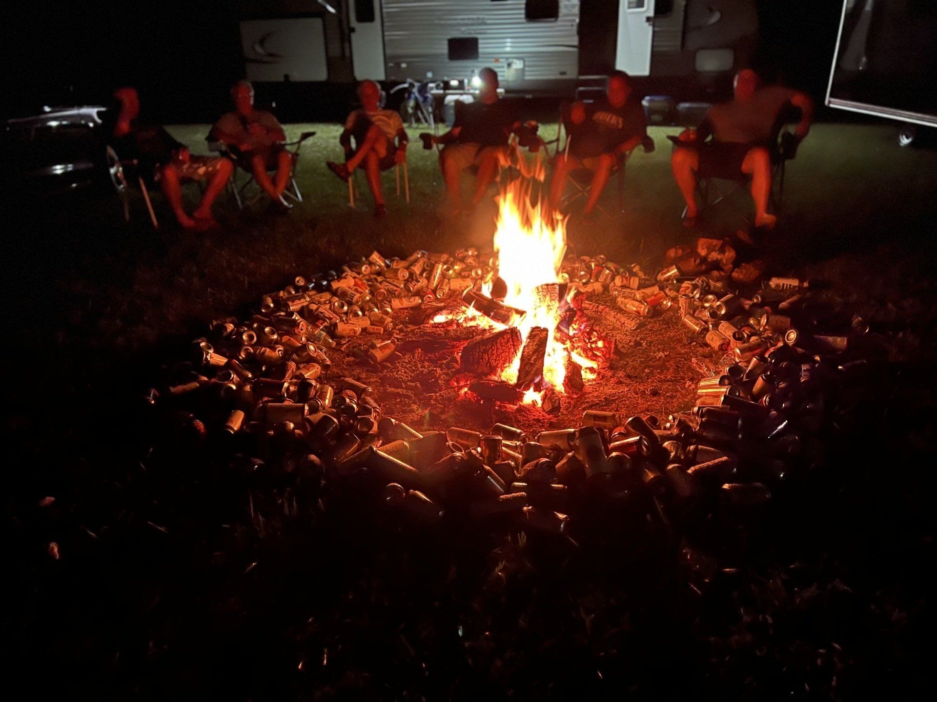 A group of people are sitting around a campfire at night.