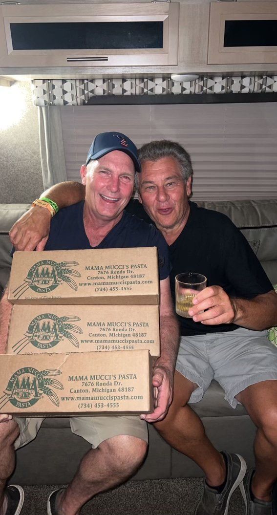 Two men are sitting on a couch holding boxes of beer.