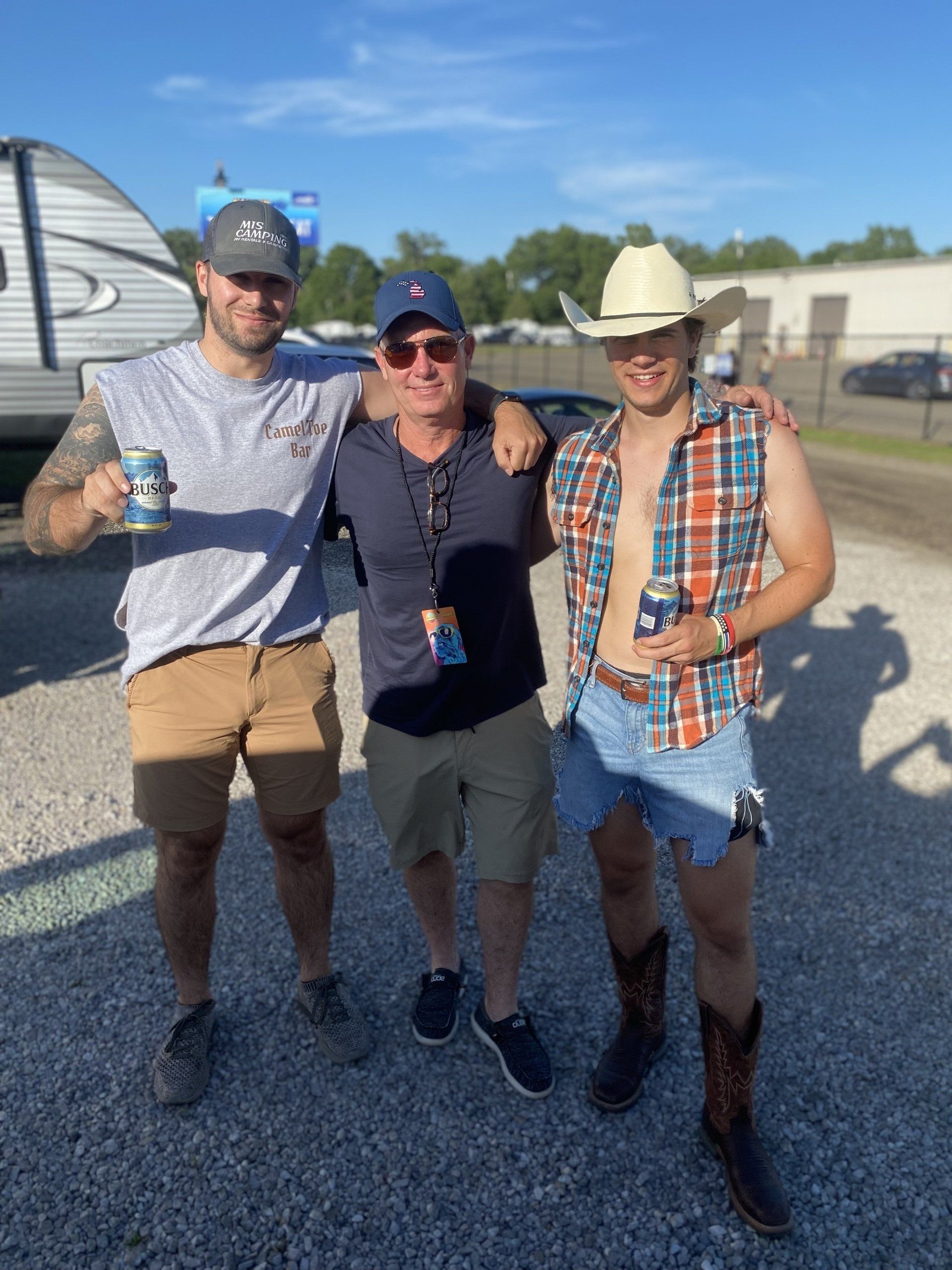 Three men are standing next to each other on a gravel road.