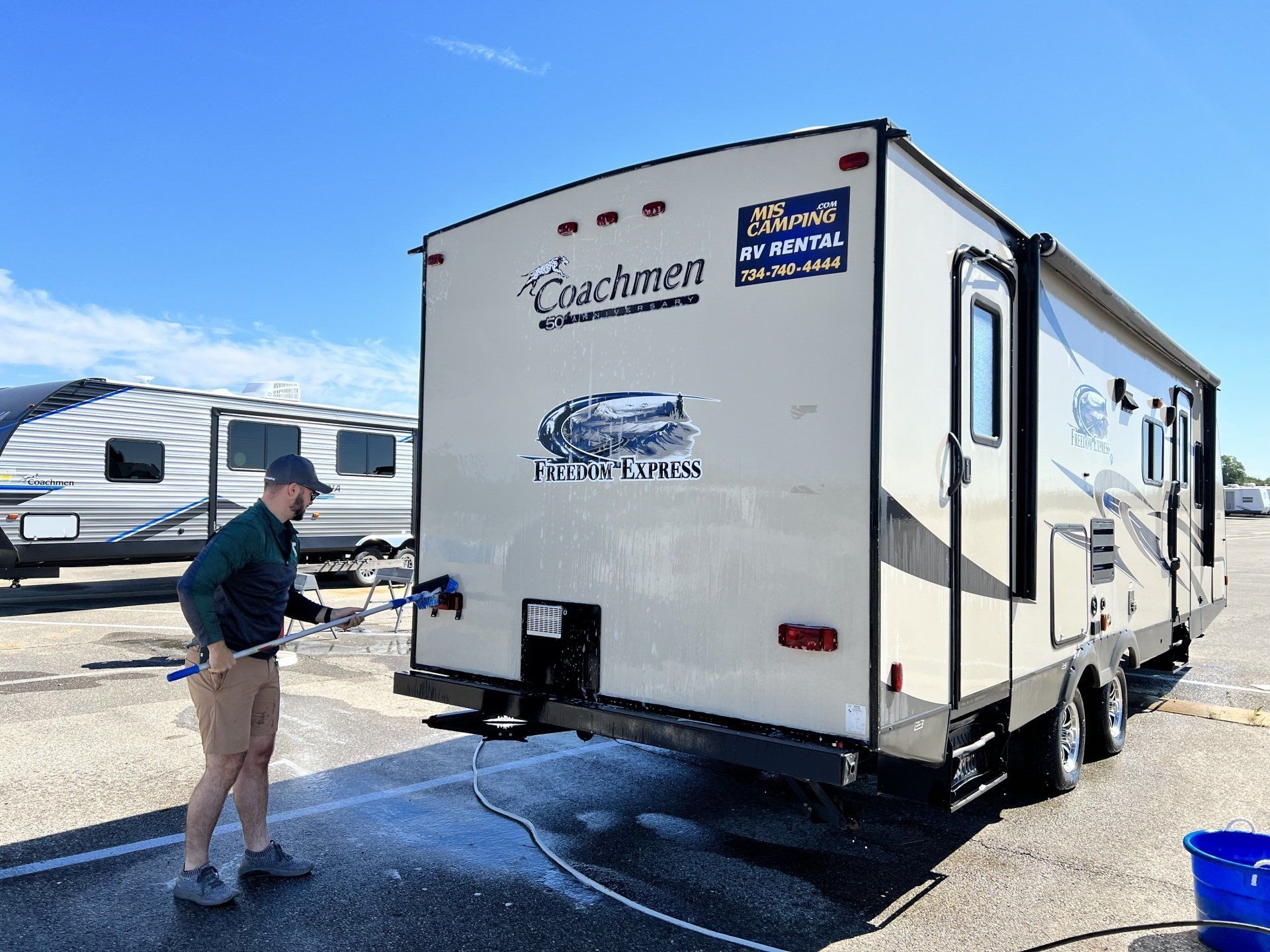 A man is washing a rv with a hose.