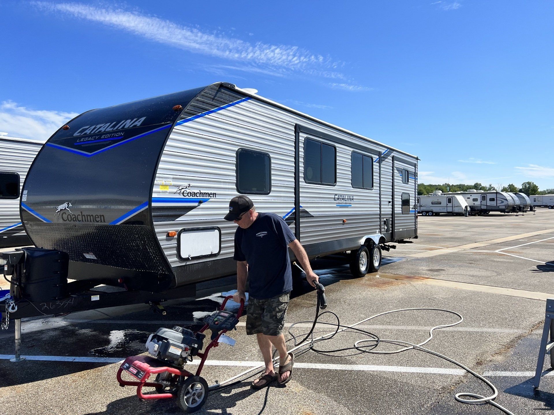 A man is washing a trailer with a pressure washer in a parking lot.