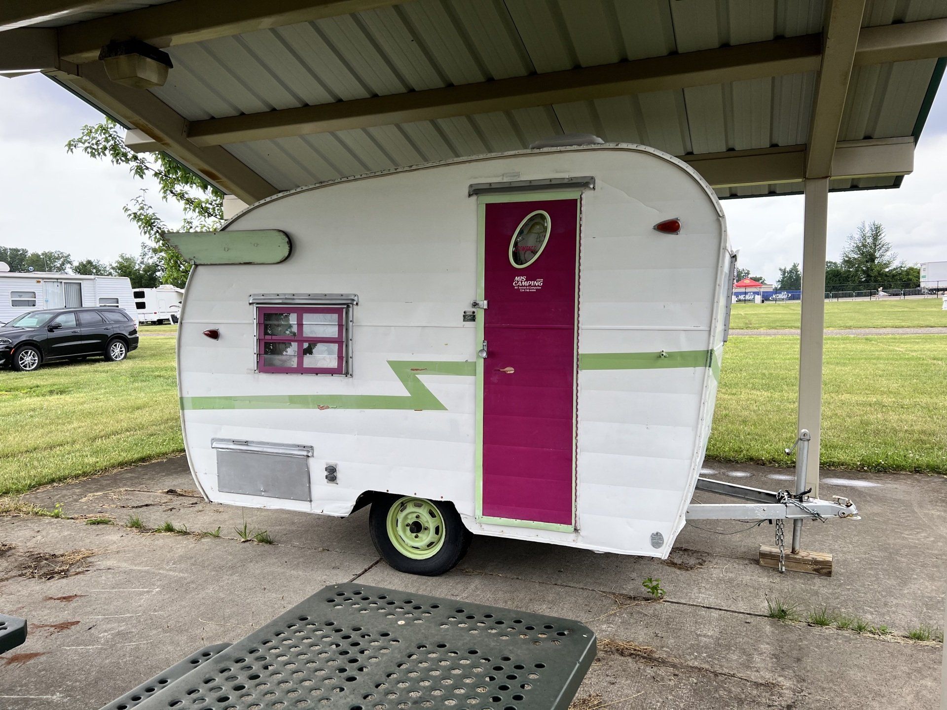 A small white trailer with a pink door is parked under a covered area.