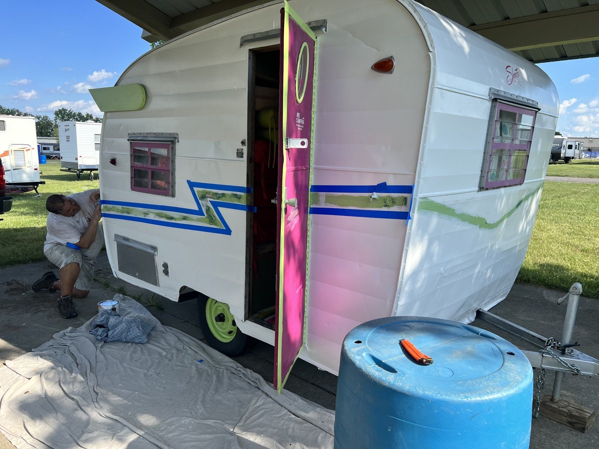 A man is painting a white trailer with a pink door.