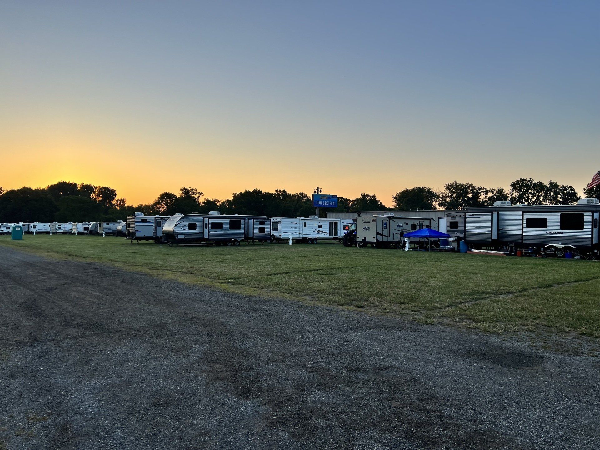 A row of rvs are parked in a field at sunset.