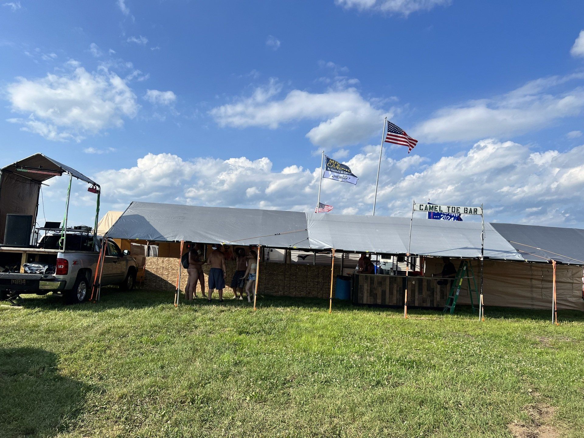 A group of people are standing under a tent in a field.