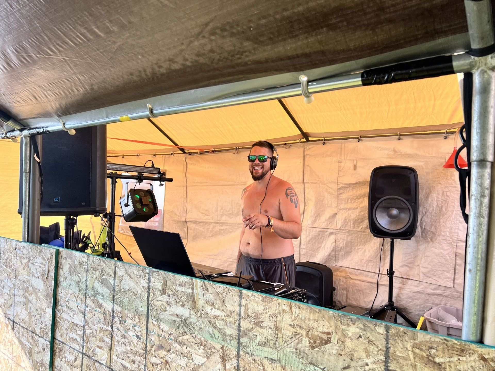 A shirtless man is playing music in a tent.