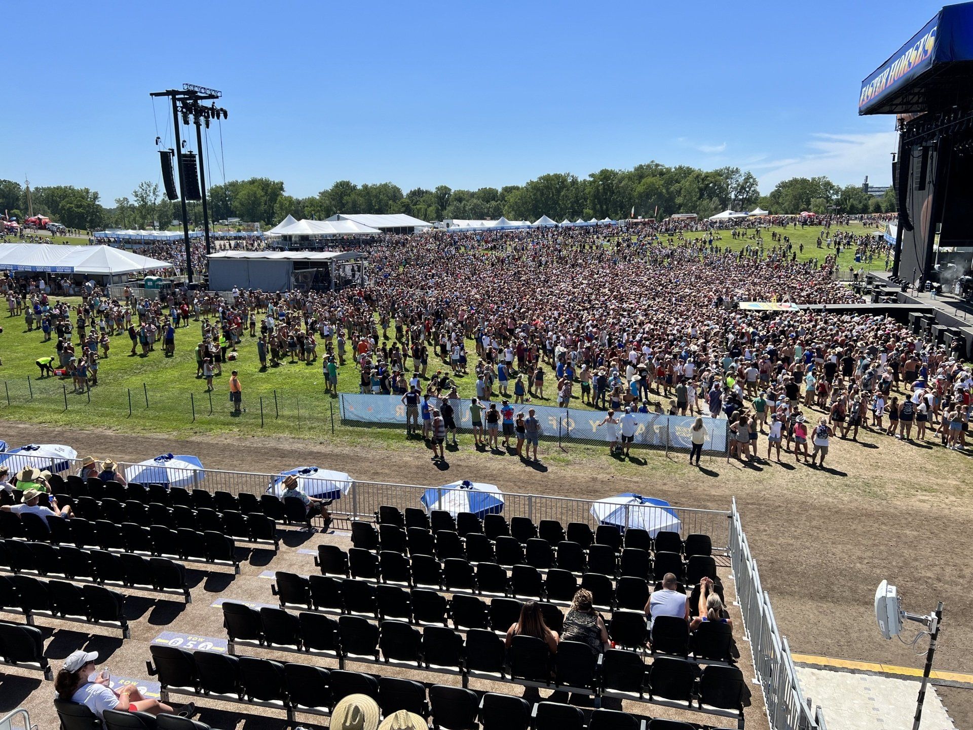 A large crowd of people are gathered in a field at a concert.