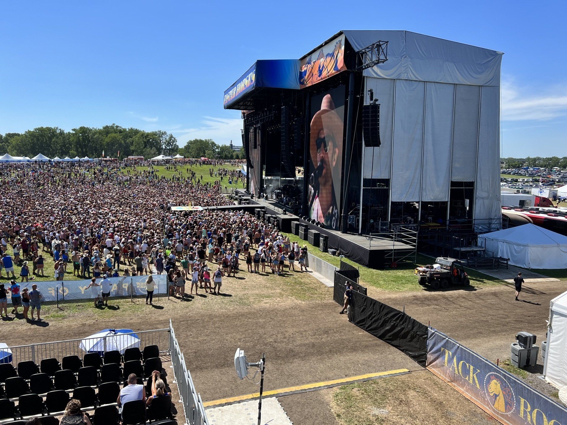 A large crowd of people are sitting in front of a large stage at a music festival.