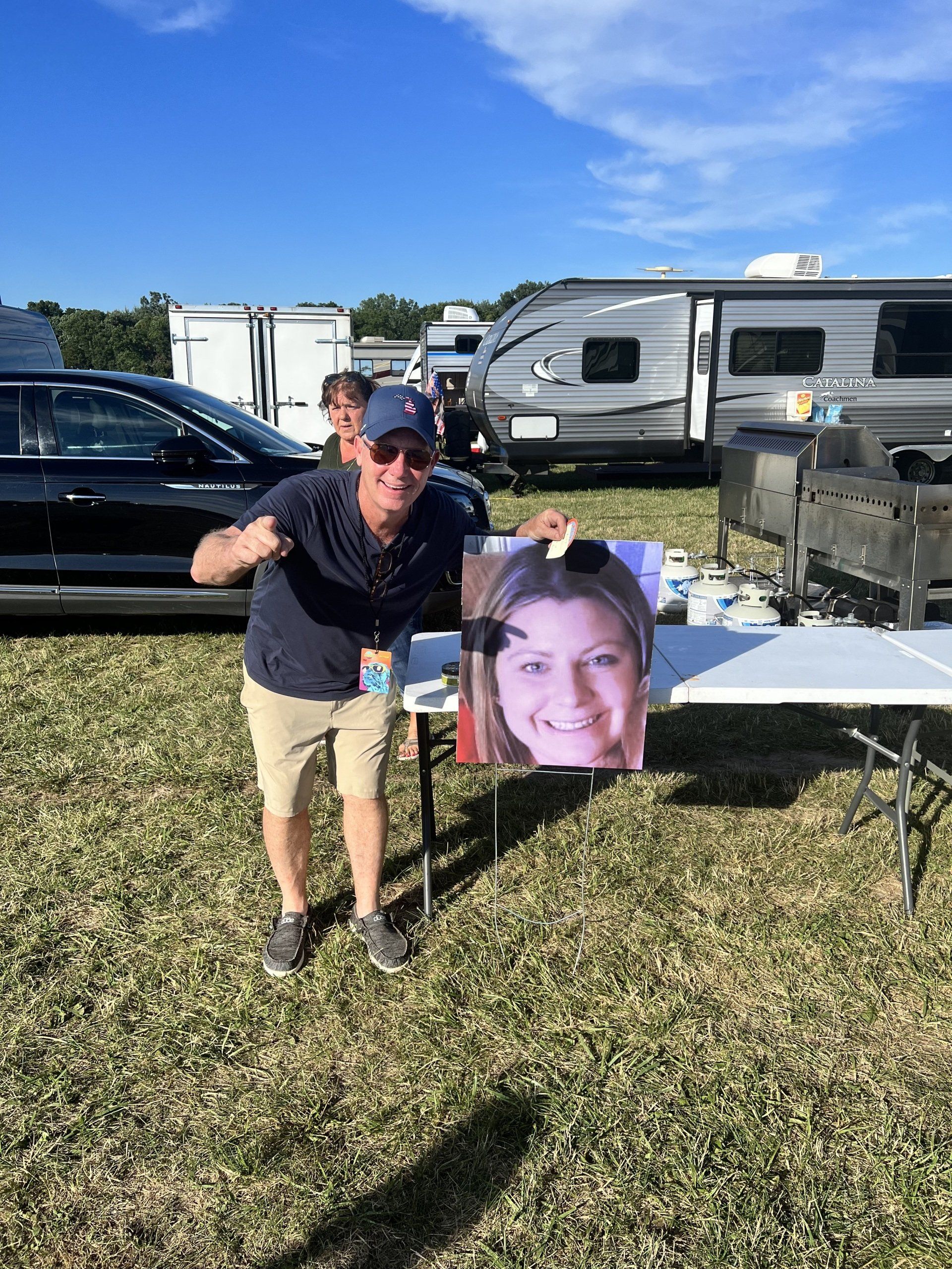 A man is standing in a field holding a picture of a woman.