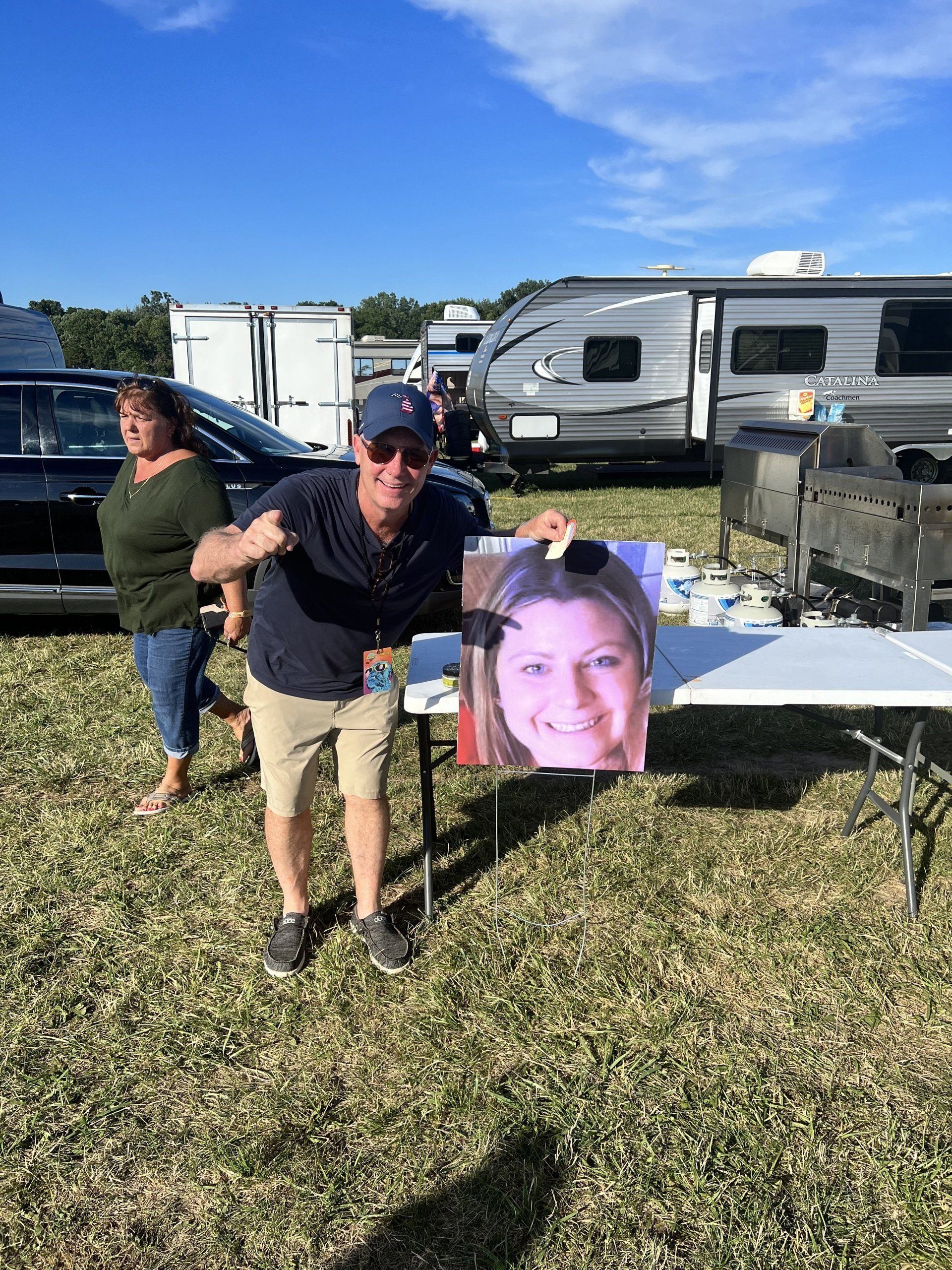 A man is holding a picture of a woman in a field.