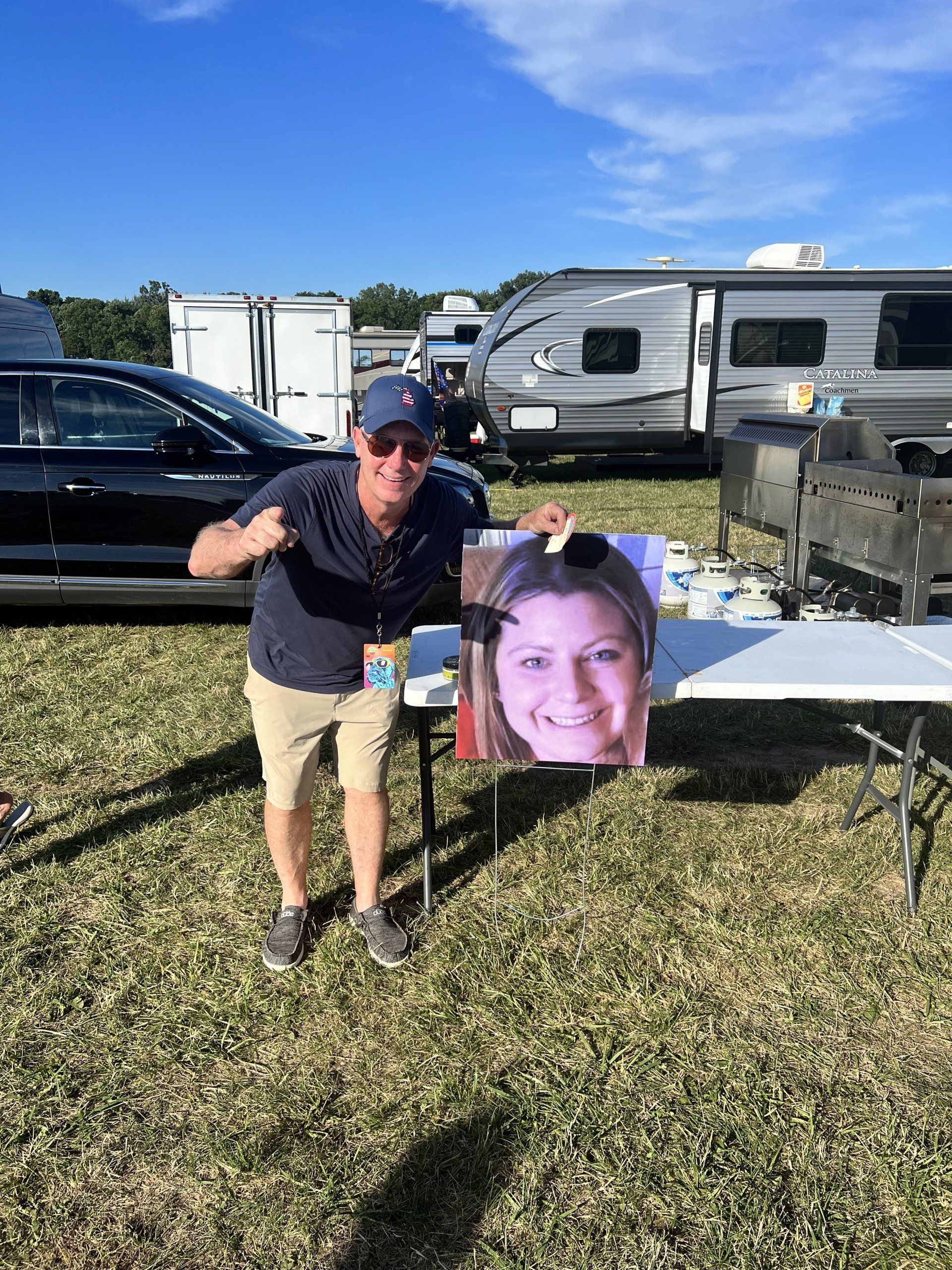 A man is standing in a field holding a picture of a woman.
