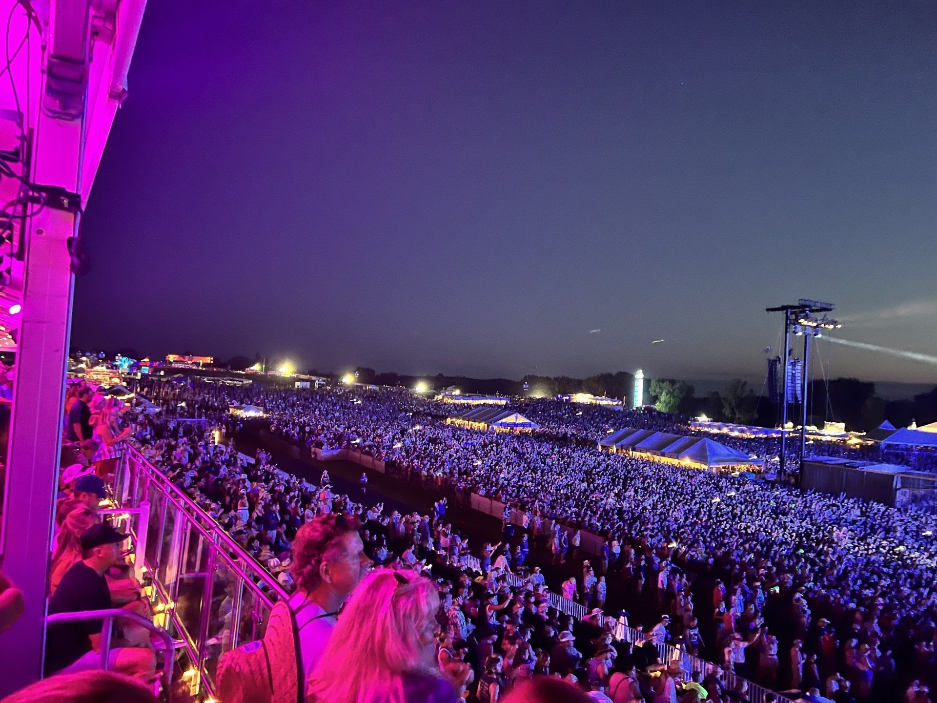A crowd of people are sitting in a stadium at a concert at night.