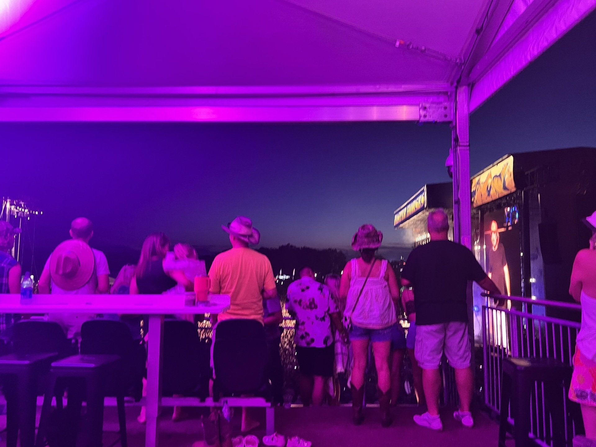 A group of people are standing under a tent with purple lights.