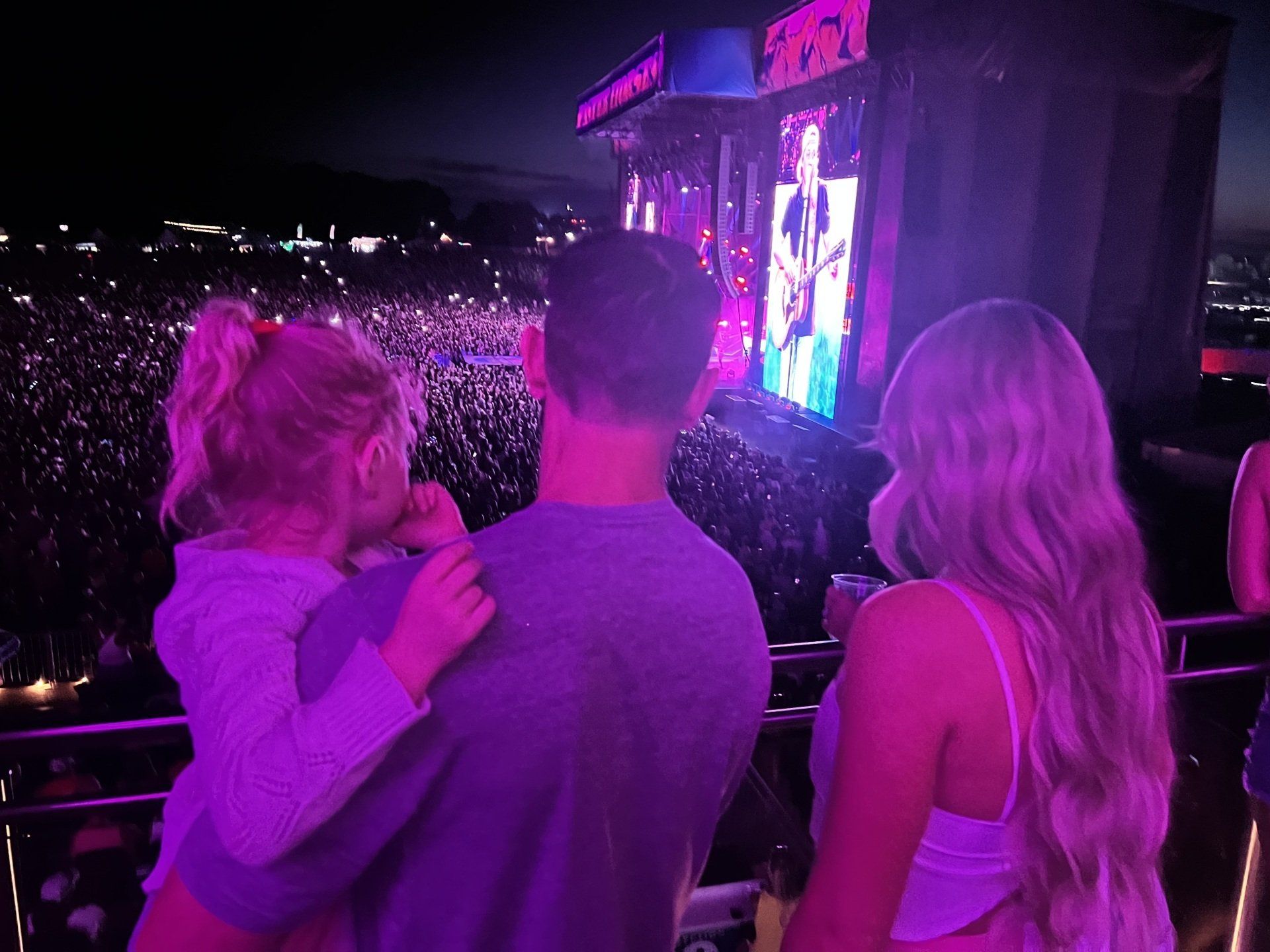 A man and two women are watching a concert at night.