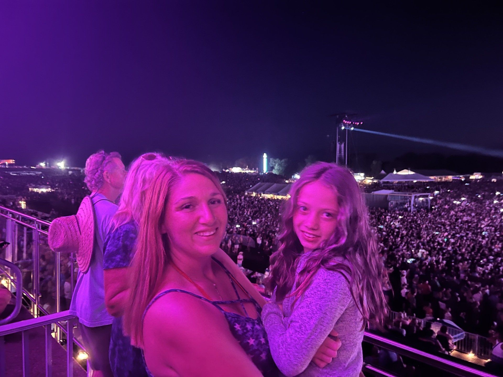 A woman and a girl are standing in front of a crowd at a concert.