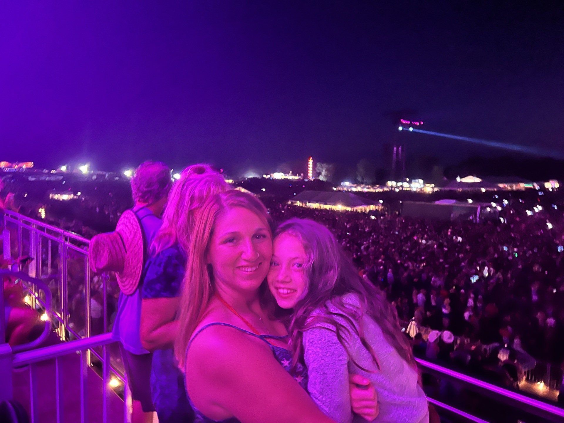 A woman and a girl are standing in front of a crowd at a concert.