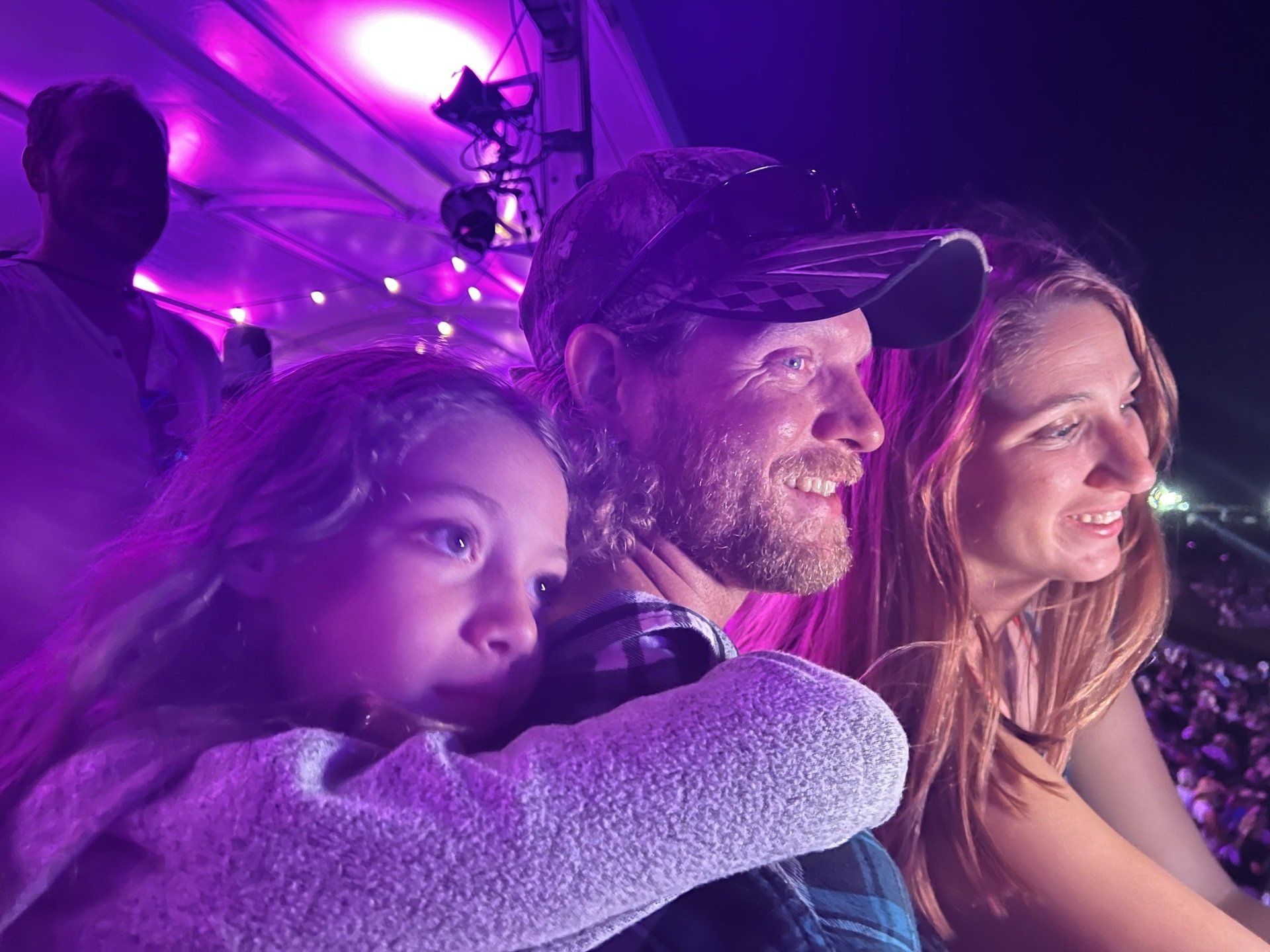 A man , woman and child are sitting in a stadium watching a concert.