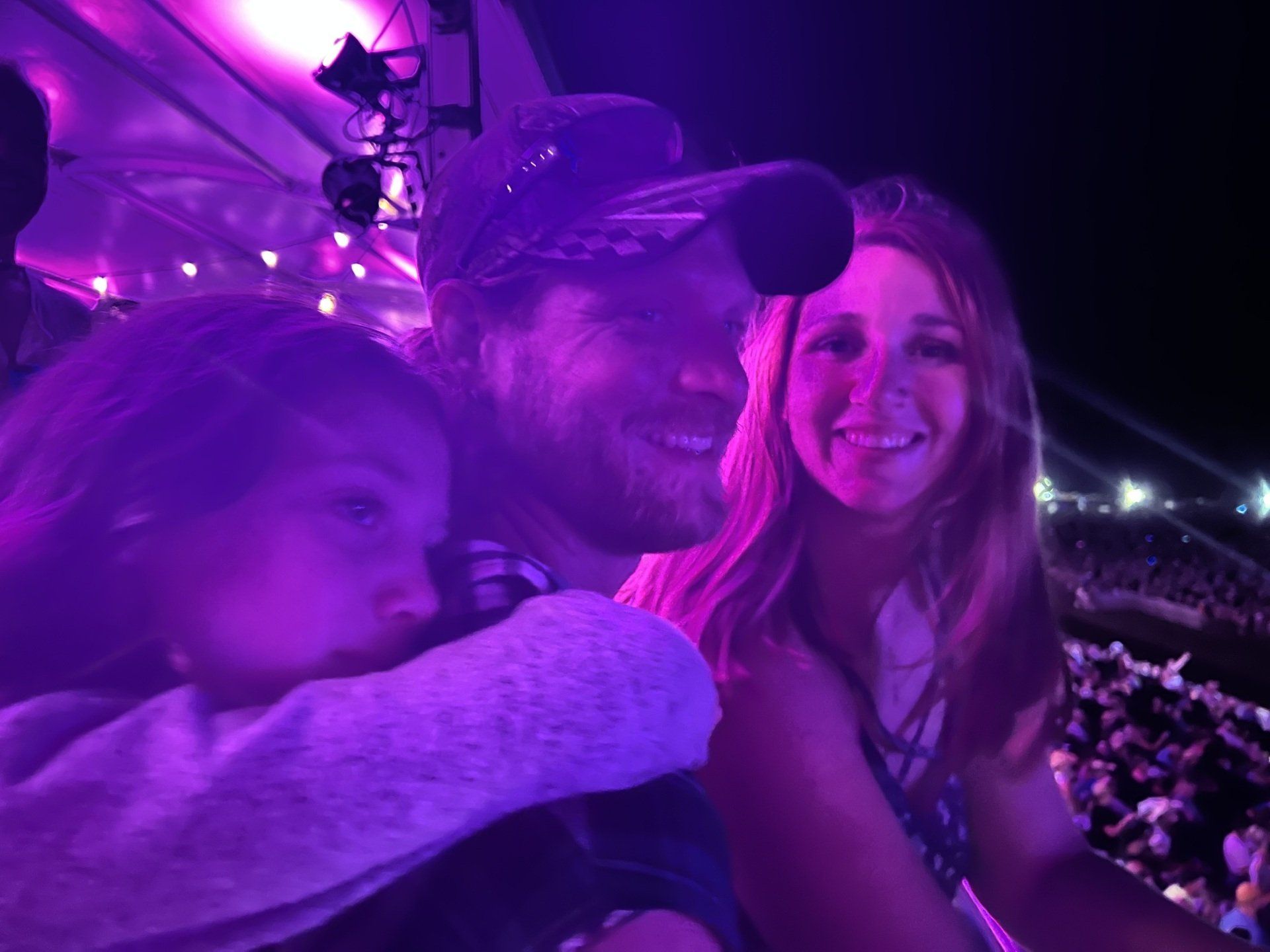 A man and two women are posing for a picture at a concert.