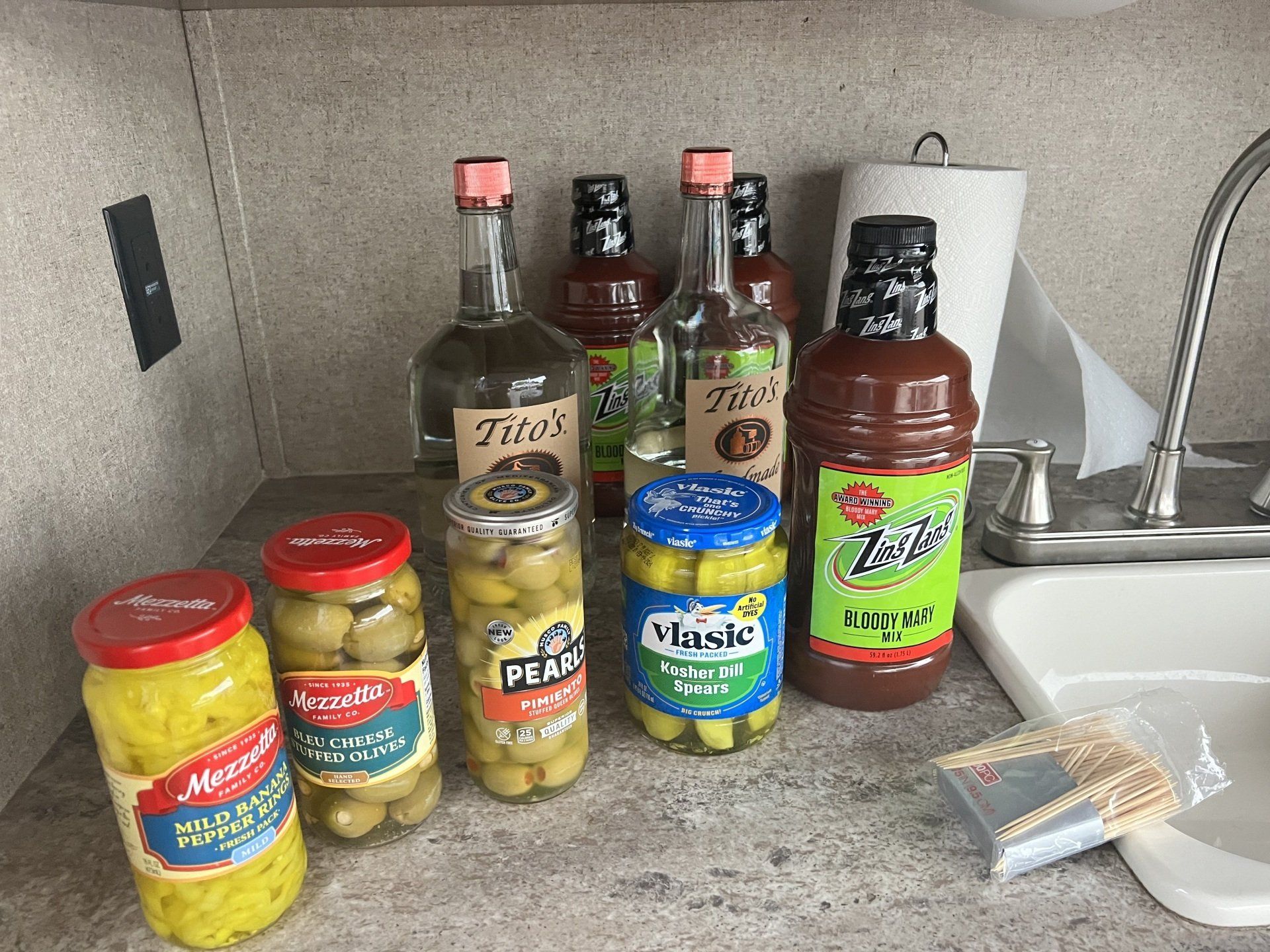 A kitchen counter with bottles of liquor , pickles , and sauce.