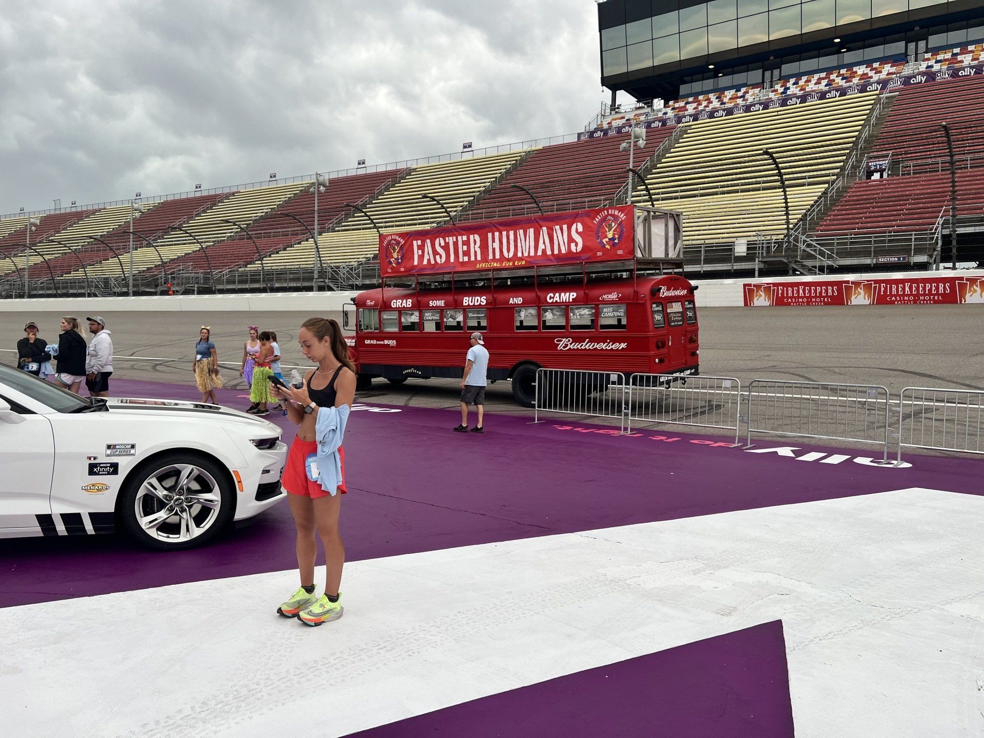 A woman is standing next to a white car on a race track.