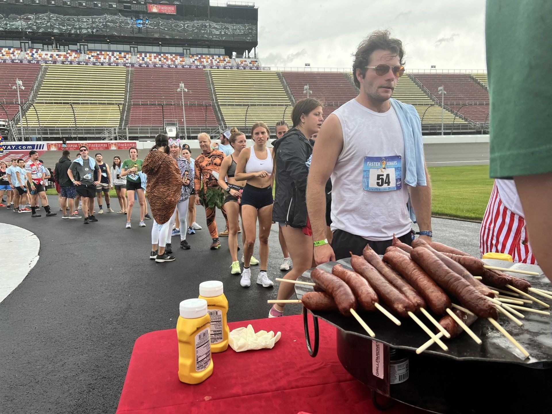 A man with the number 04 on his shirt is standing next to a table with sausages on sticks