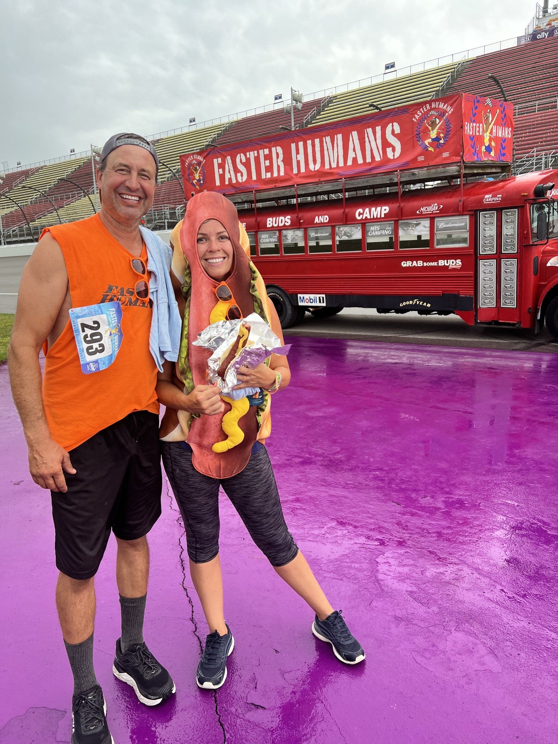 A man and a woman are standing in front of a red bus that says faster humans